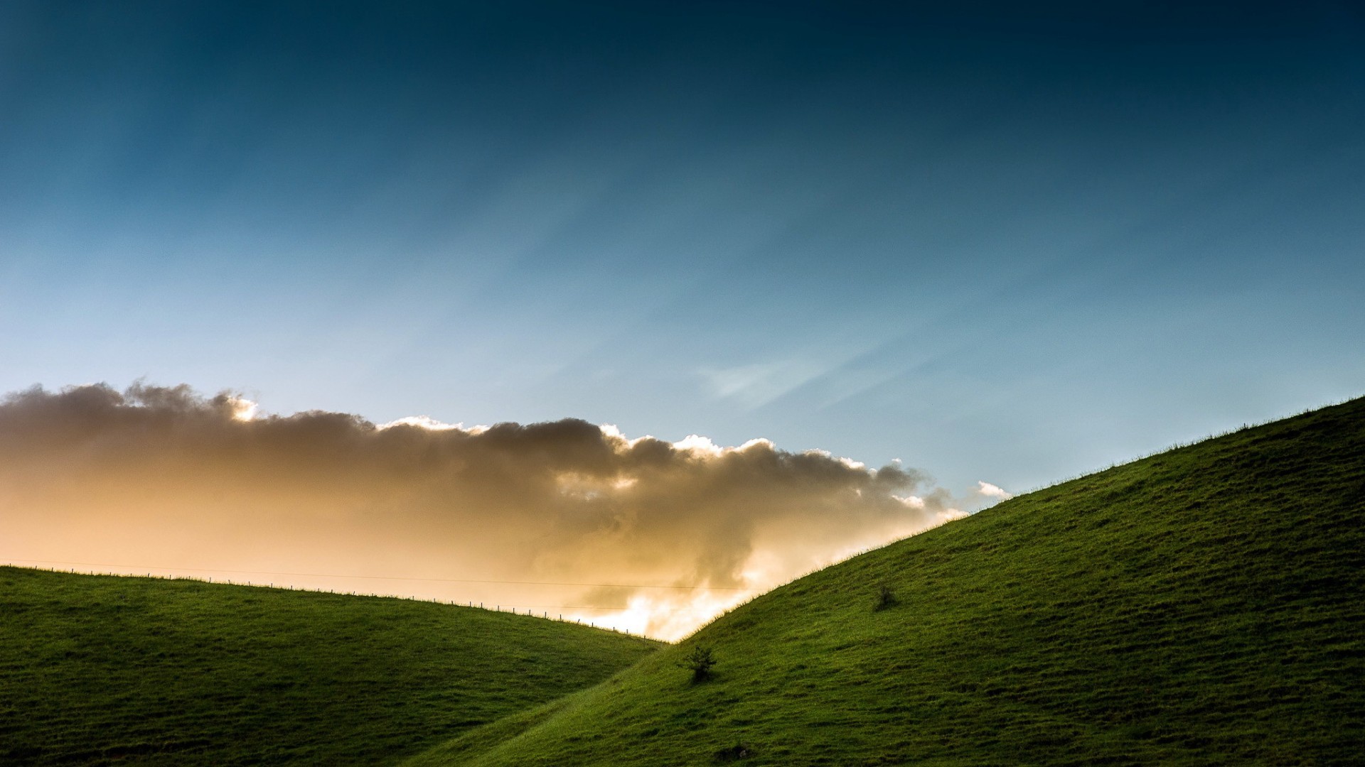 Green hills under a cloudy sky with sun rays HD Wallpaper
