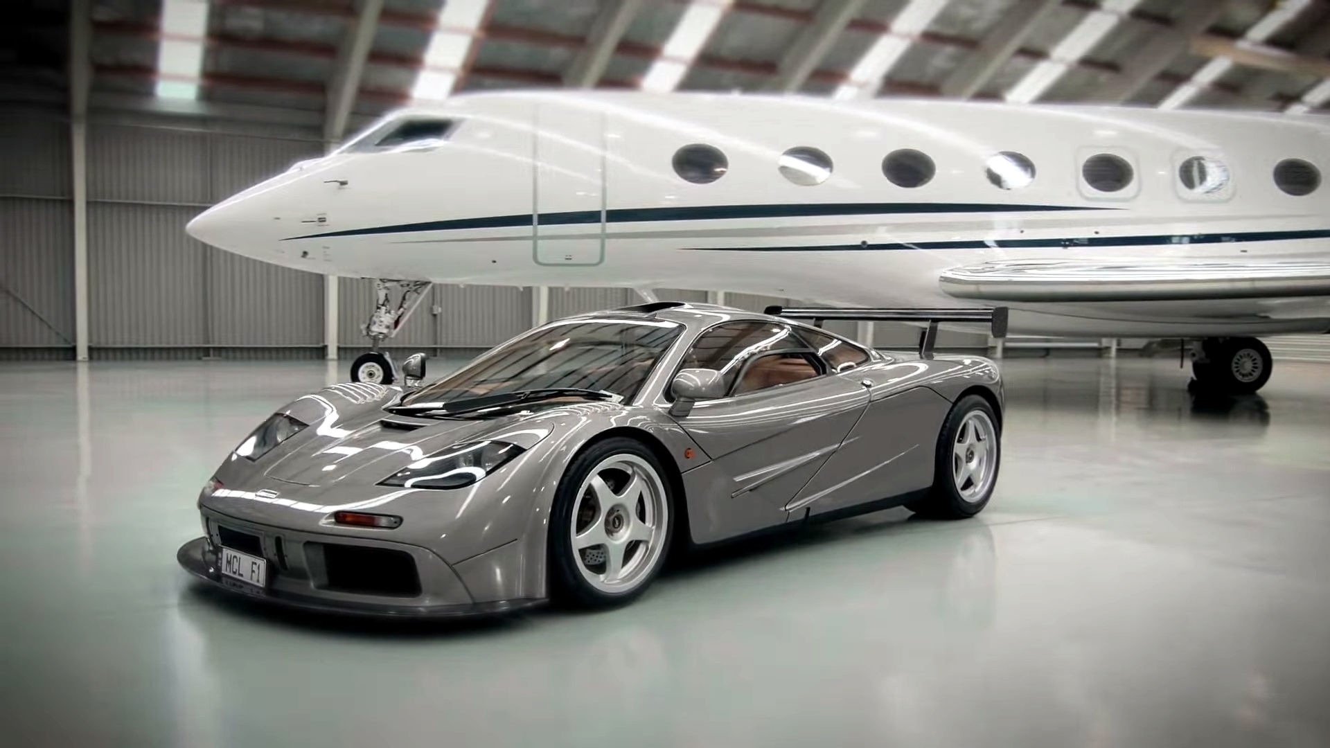McLaren F1 car and private jet in a hangar HD Wallpaper