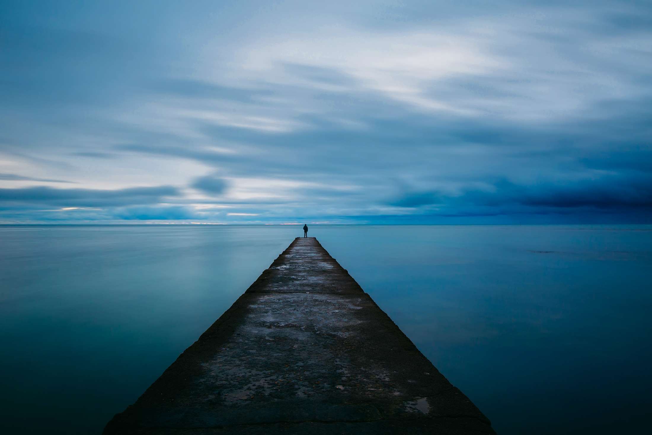 Lone figure on a pier at dusk over the ocean HD Wallpaper