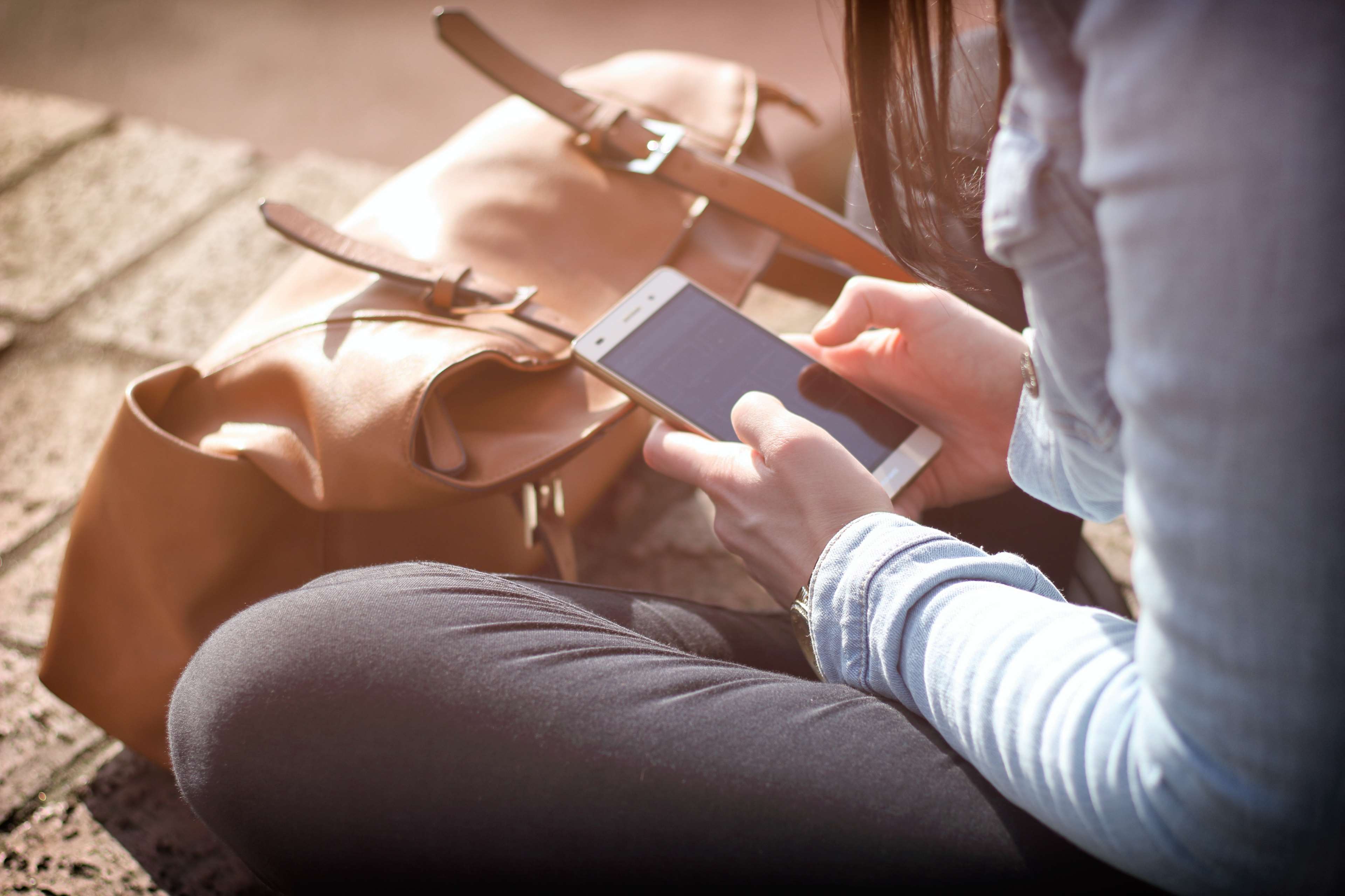 Woman sitting and using a smartphone with a bag HD Wallpaper