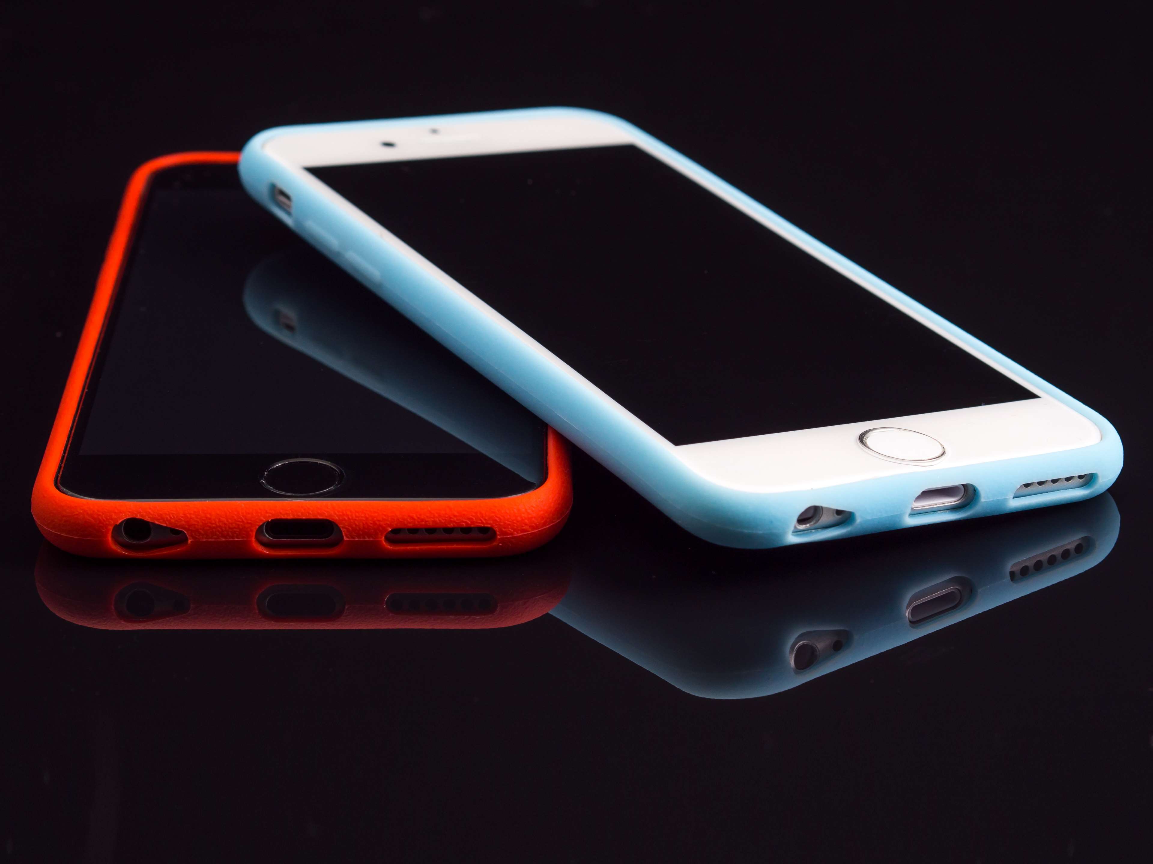 Two iPhones with colorful cases on a reflective surface HD Wallpaper