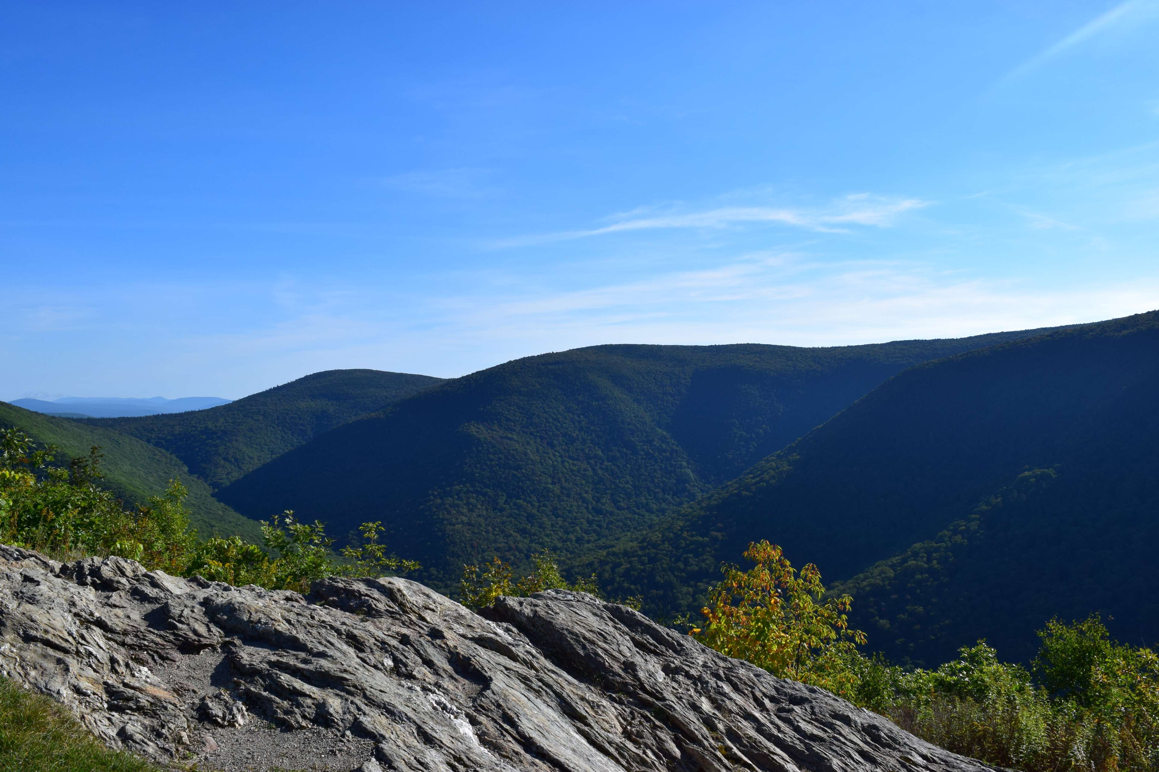 Mountain valley with rocky foreground under blue sky HD Wallpaper