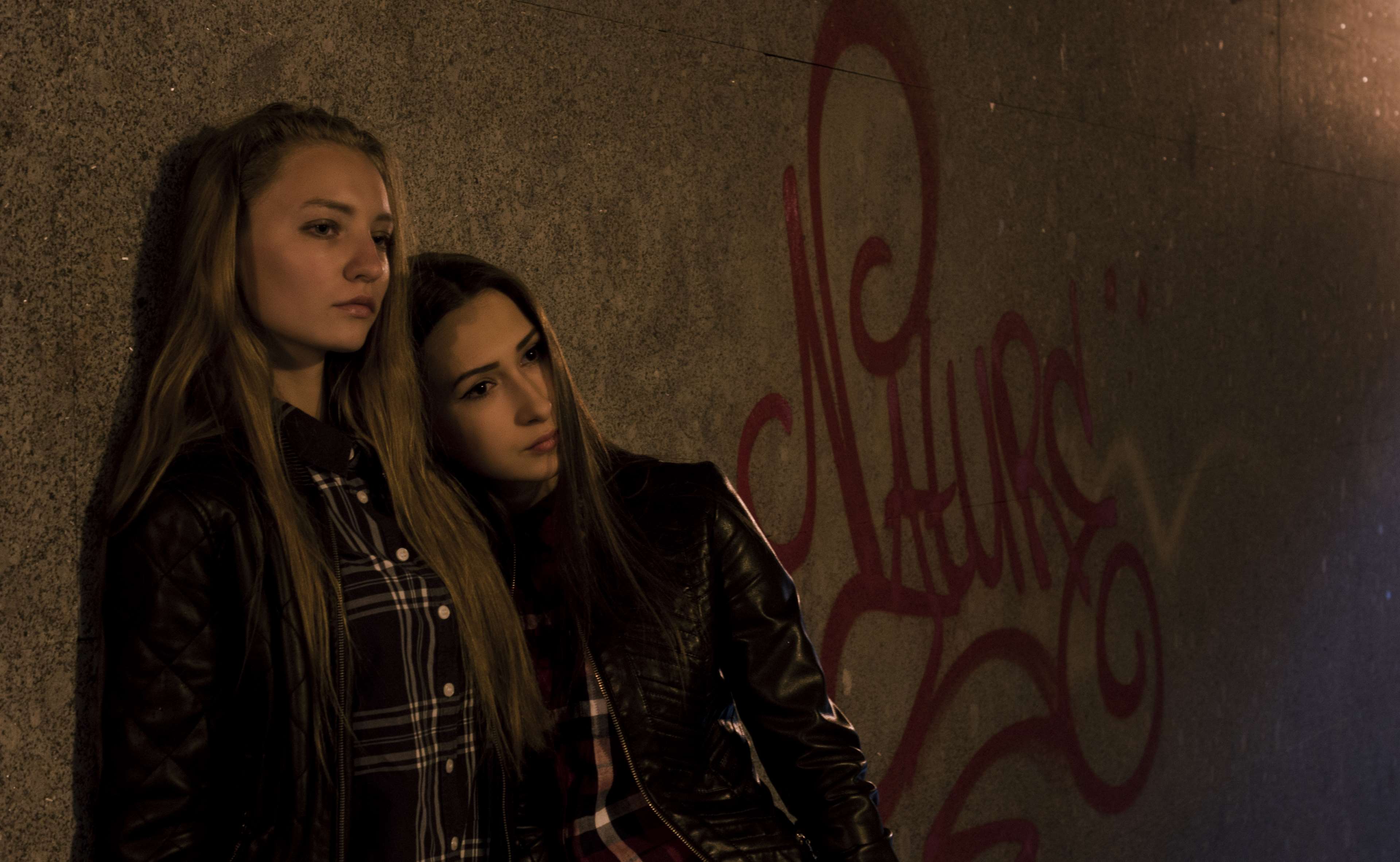 Two young women leaning against a graffiti-covered wall at night HD Wallpaper