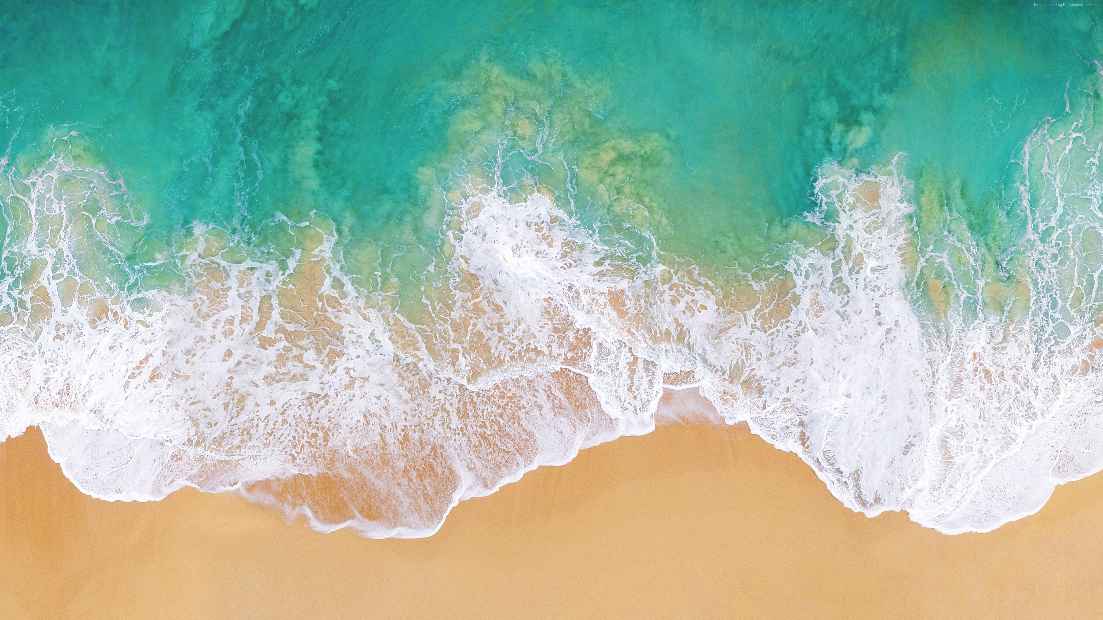 Aerial view of ocean waves crashing on a sandy beach HD Wallpaper