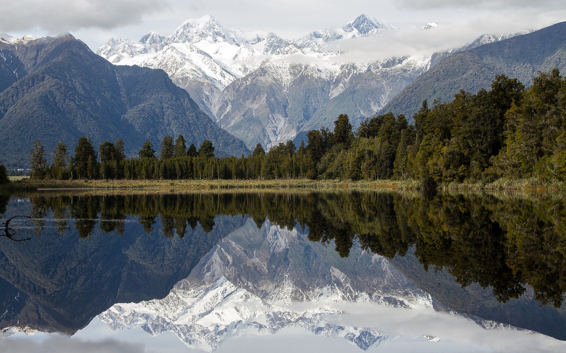 Snow-capped mountains reflected in a lake with trees HD Wallpaper