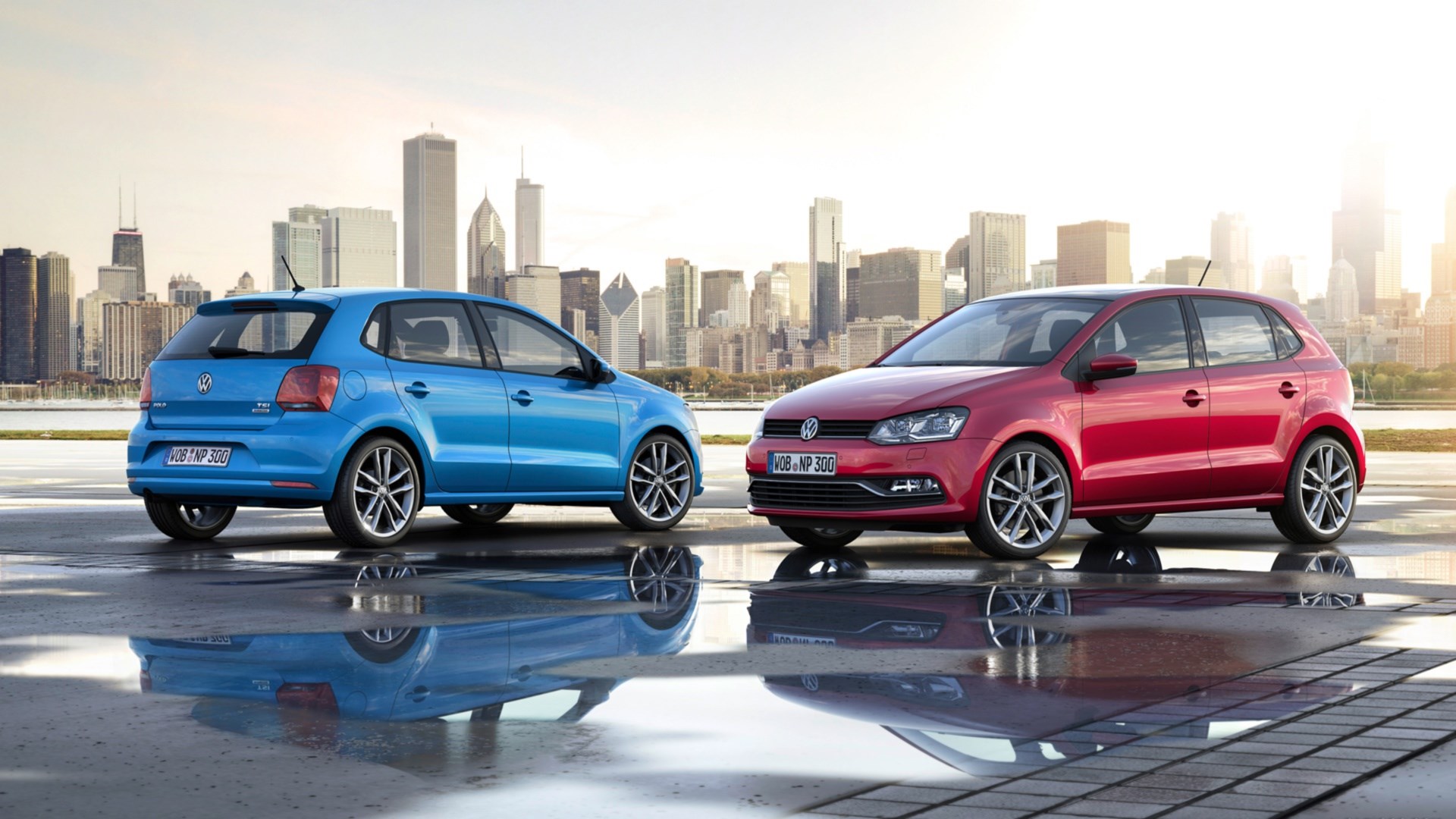 Two Volkswagen Polo cars parked by a city skyline HD Wallpaper