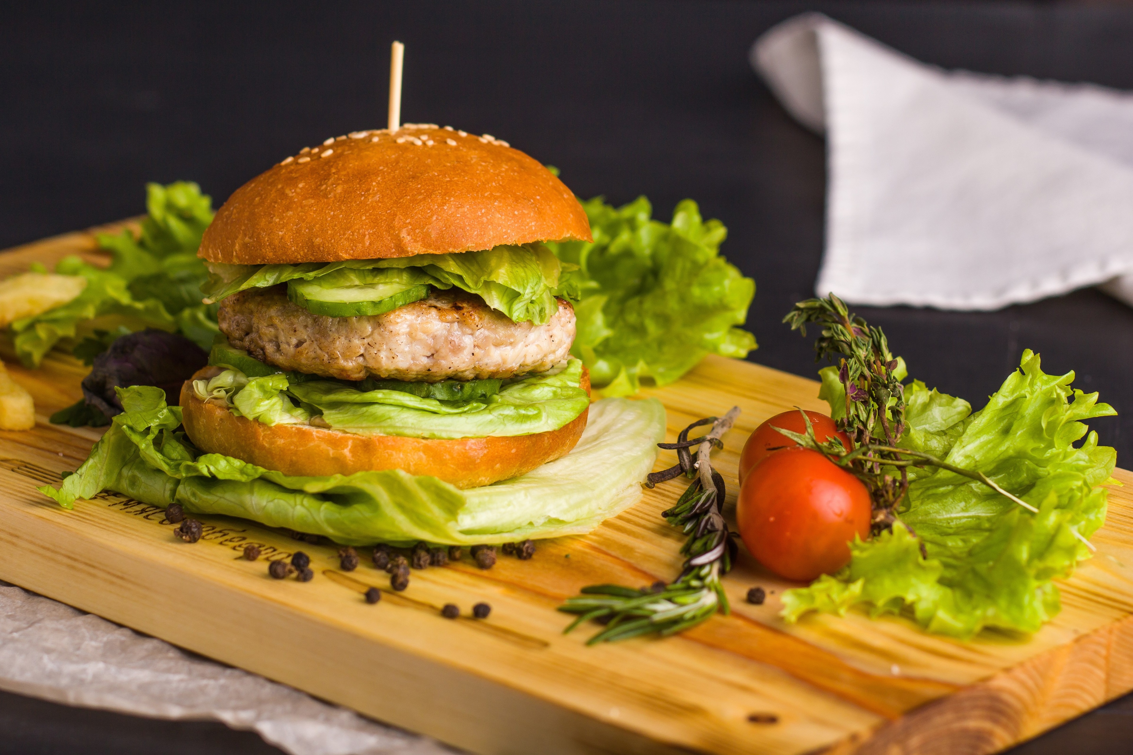 Burger with lettuce, cucumber, tomato, and herbs on a wooden board HD Wallpaper