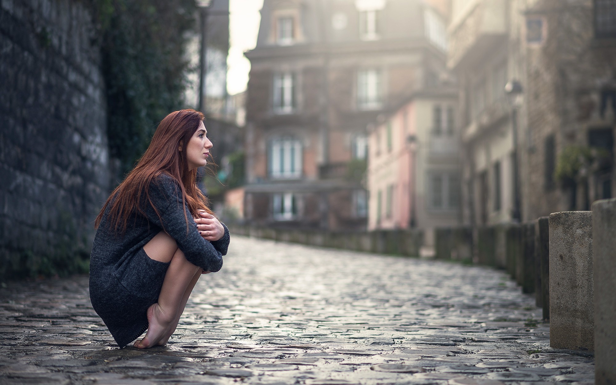 Barefoot woman crouching on cobblestone street in urban town HD Wallpaper
