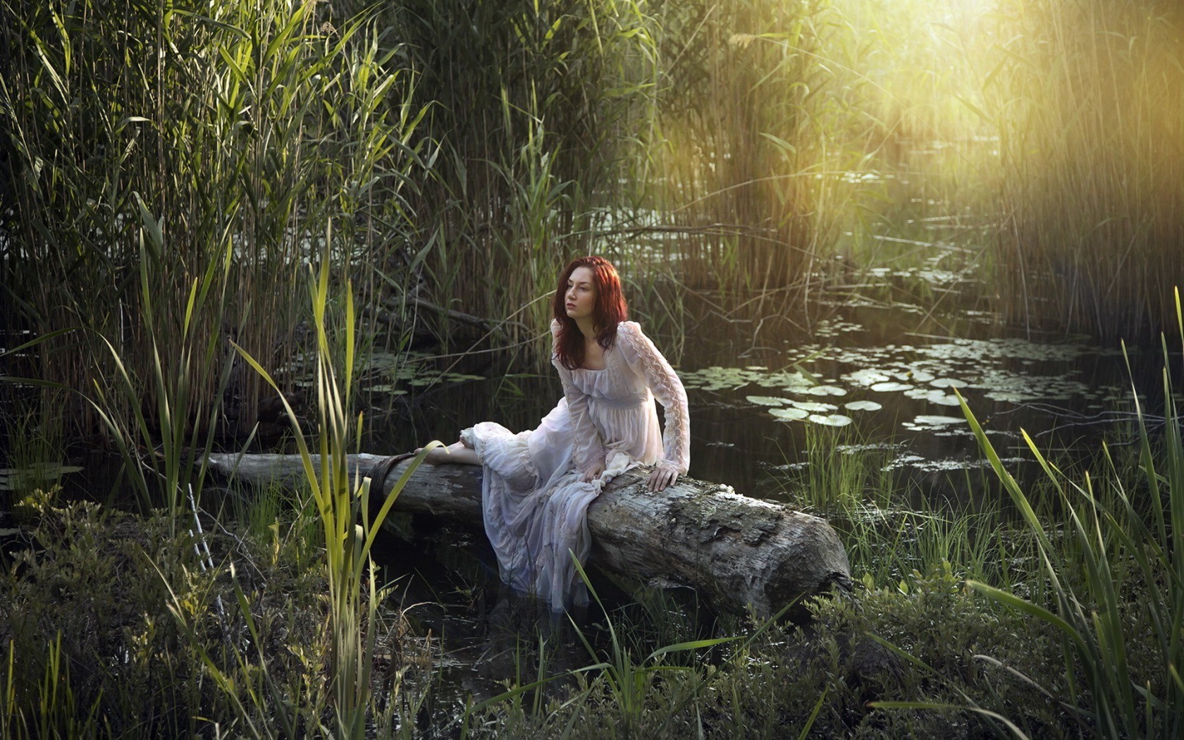 Woman in a white dress sitting on a log in a swamp HD Wallpaper