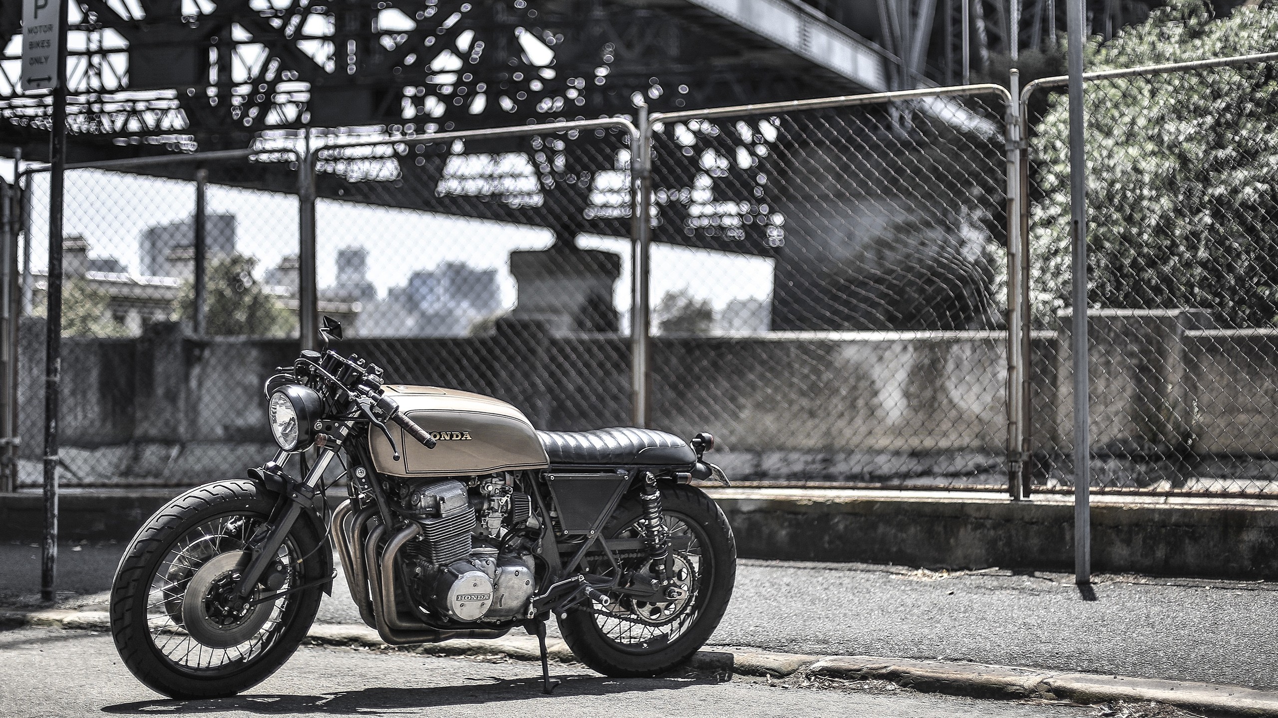 Honda motorcycle parked near a chain-link fence and bridge HD Wallpaper