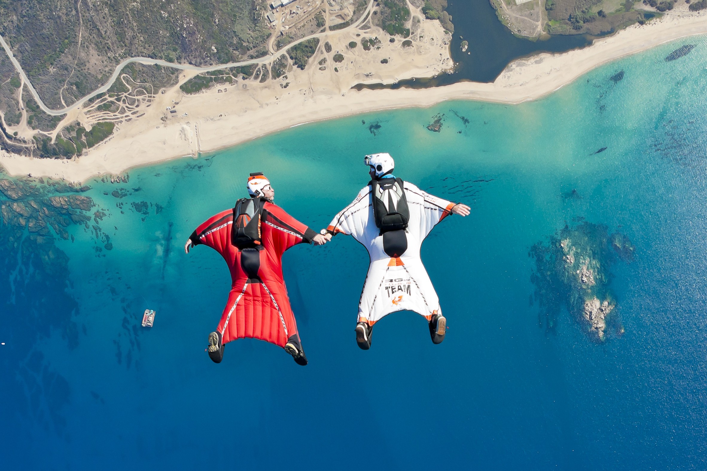 Two skydivers in wingsuits over a beach and sea HD Wallpaper