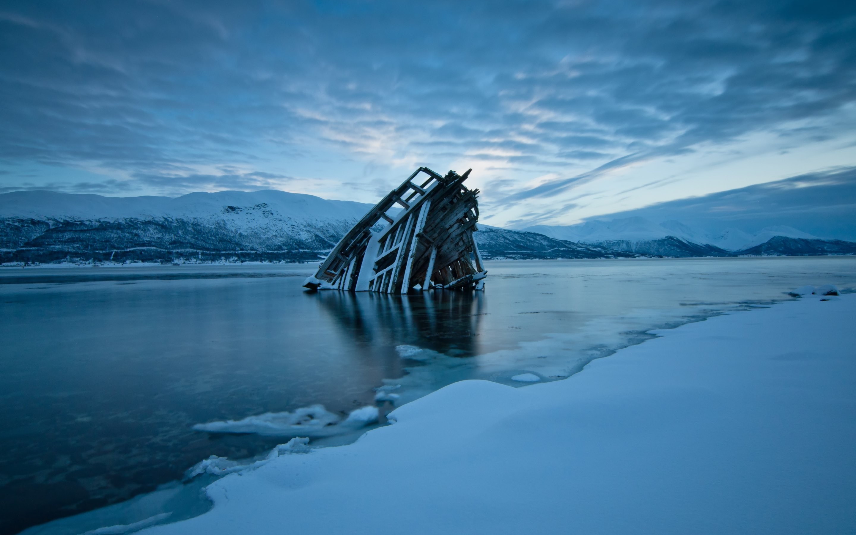 Shipwreck in a frozen lake with snow-covered mountains HD Wallpaper