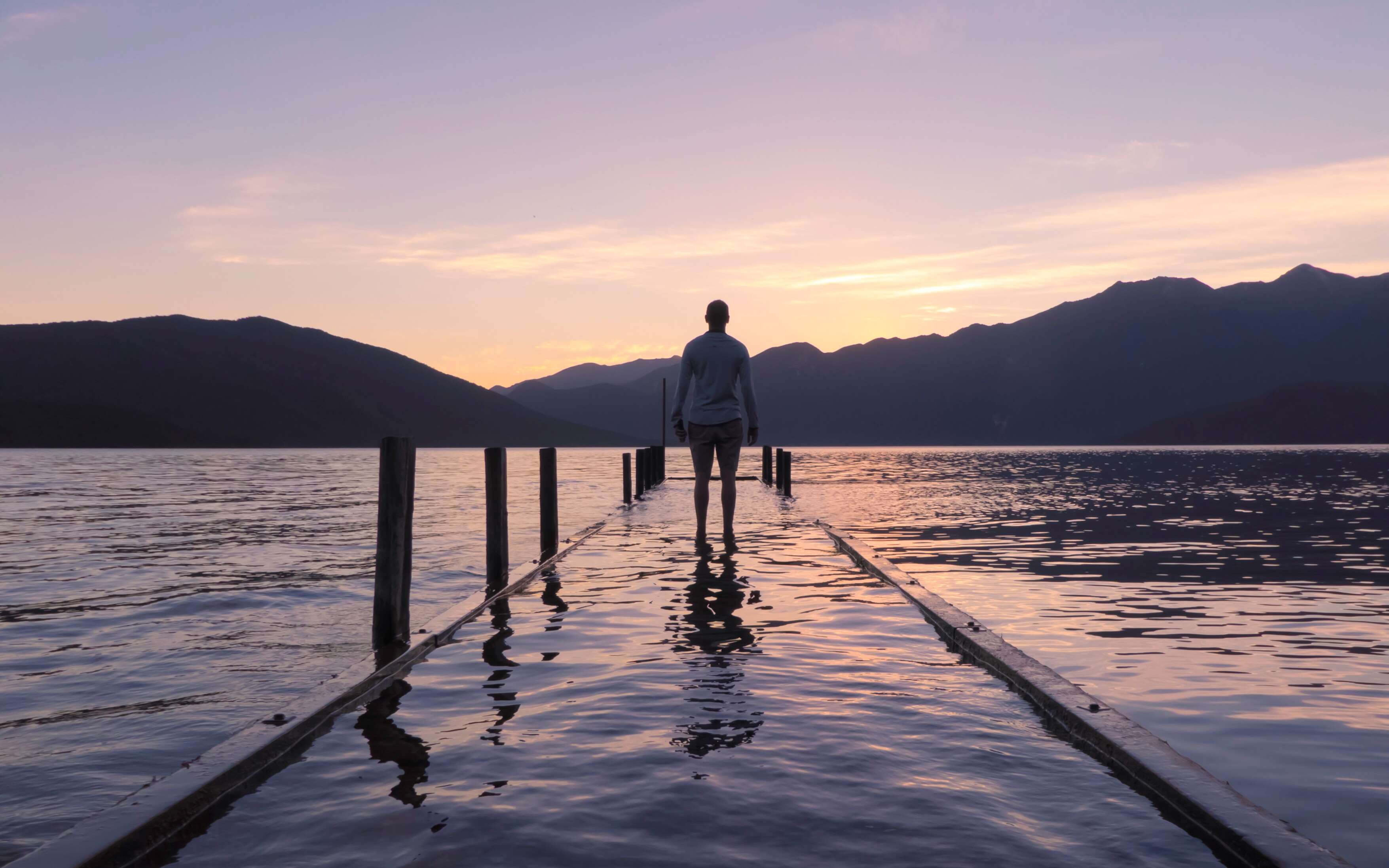 Man standing on a dock at sunset over a lake HD Wallpaper
