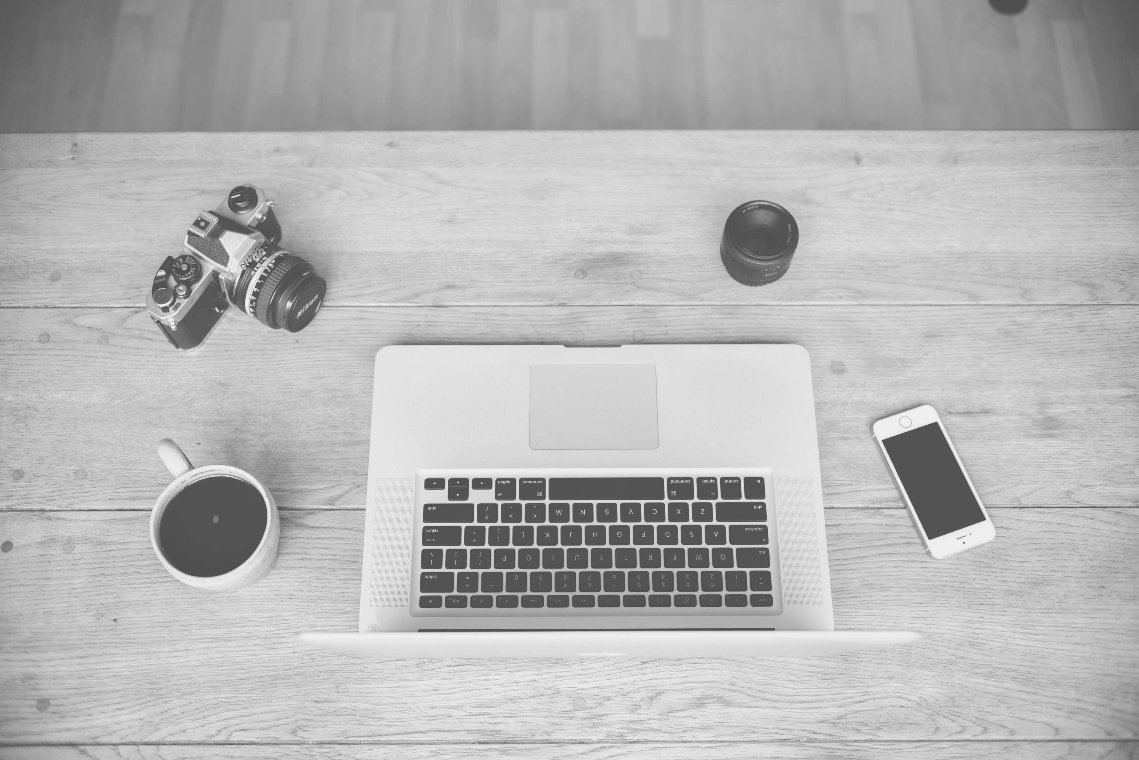 Overhead view of a photographer's desk with MacBook Pro, camera, coffee, and phone HD Wallpaper