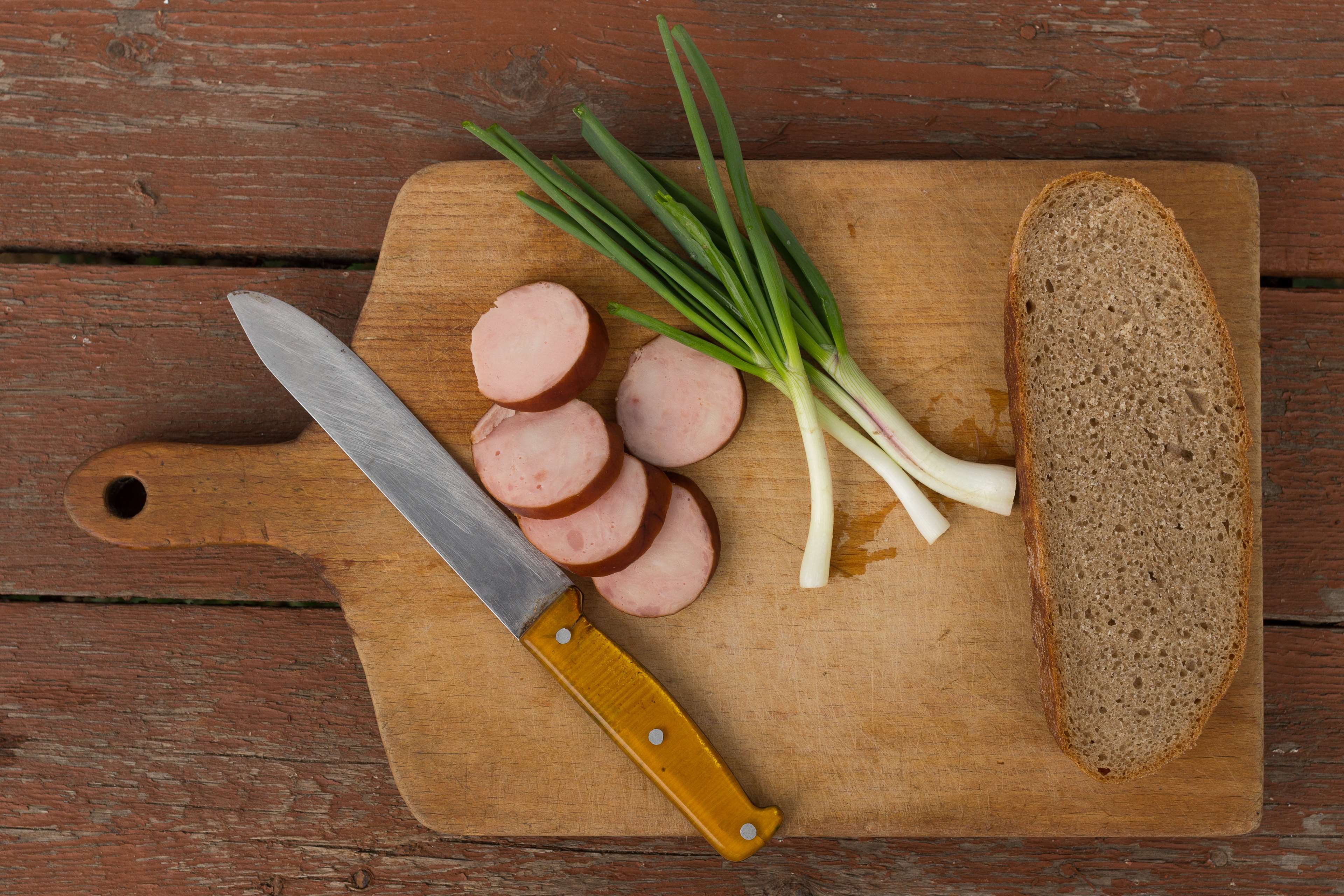 Sausage, green onions, and bread on a chopping board with a knife HD Wallpaper