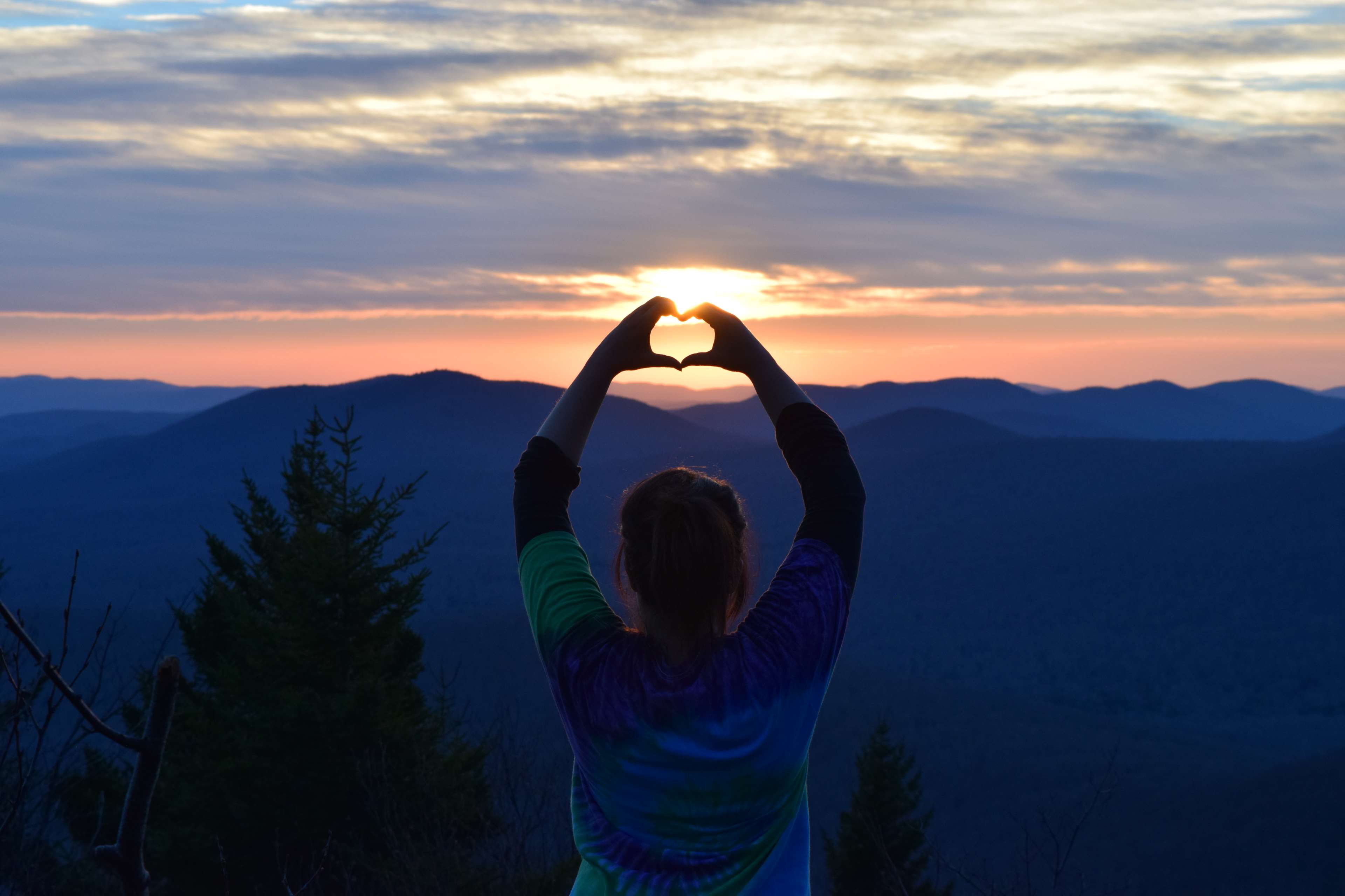 Woman making heart shape with hands at sunset over mountains HD Wallpaper