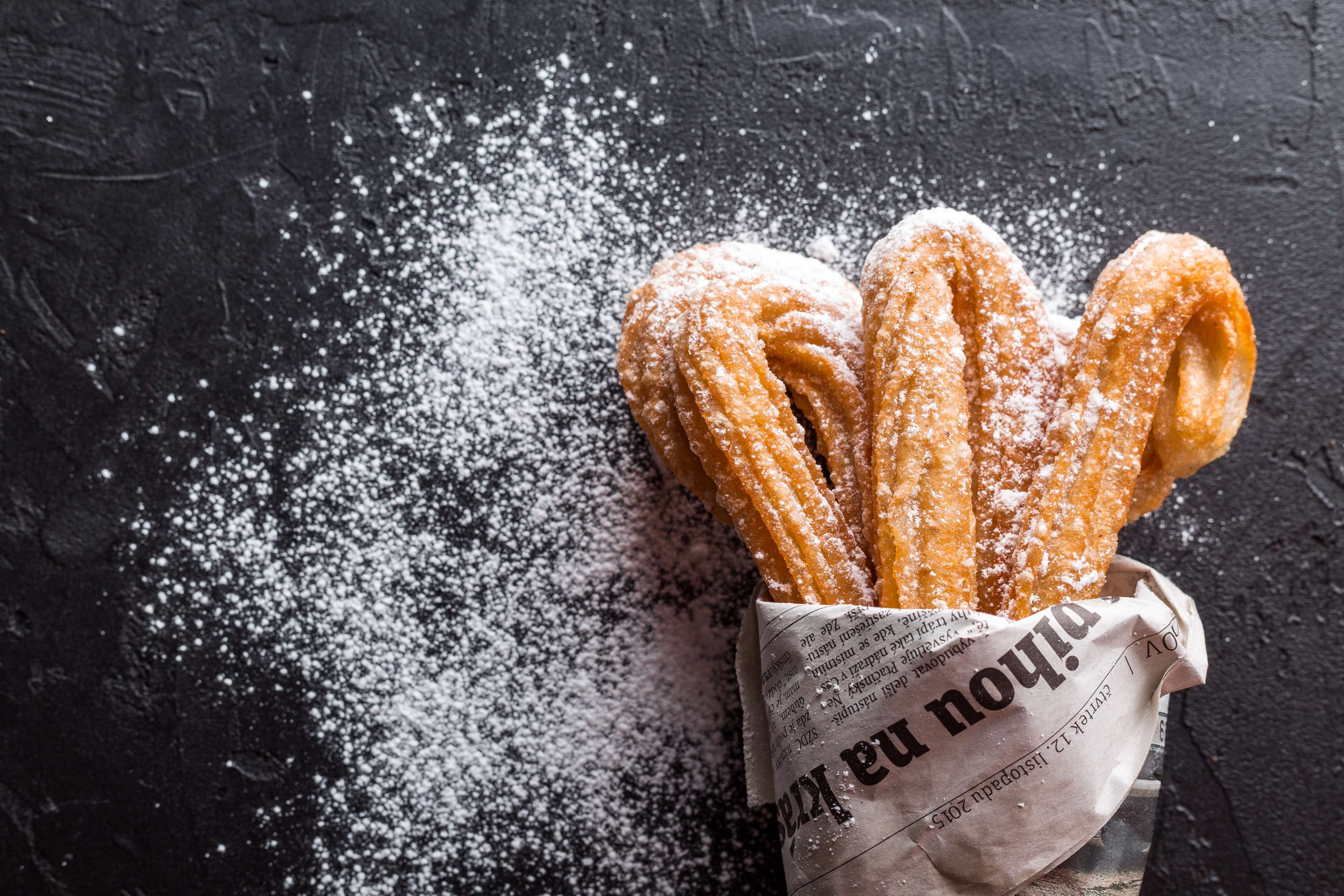 Churros dusted with powdered sugar in a newspaper cone HD Wallpaper
