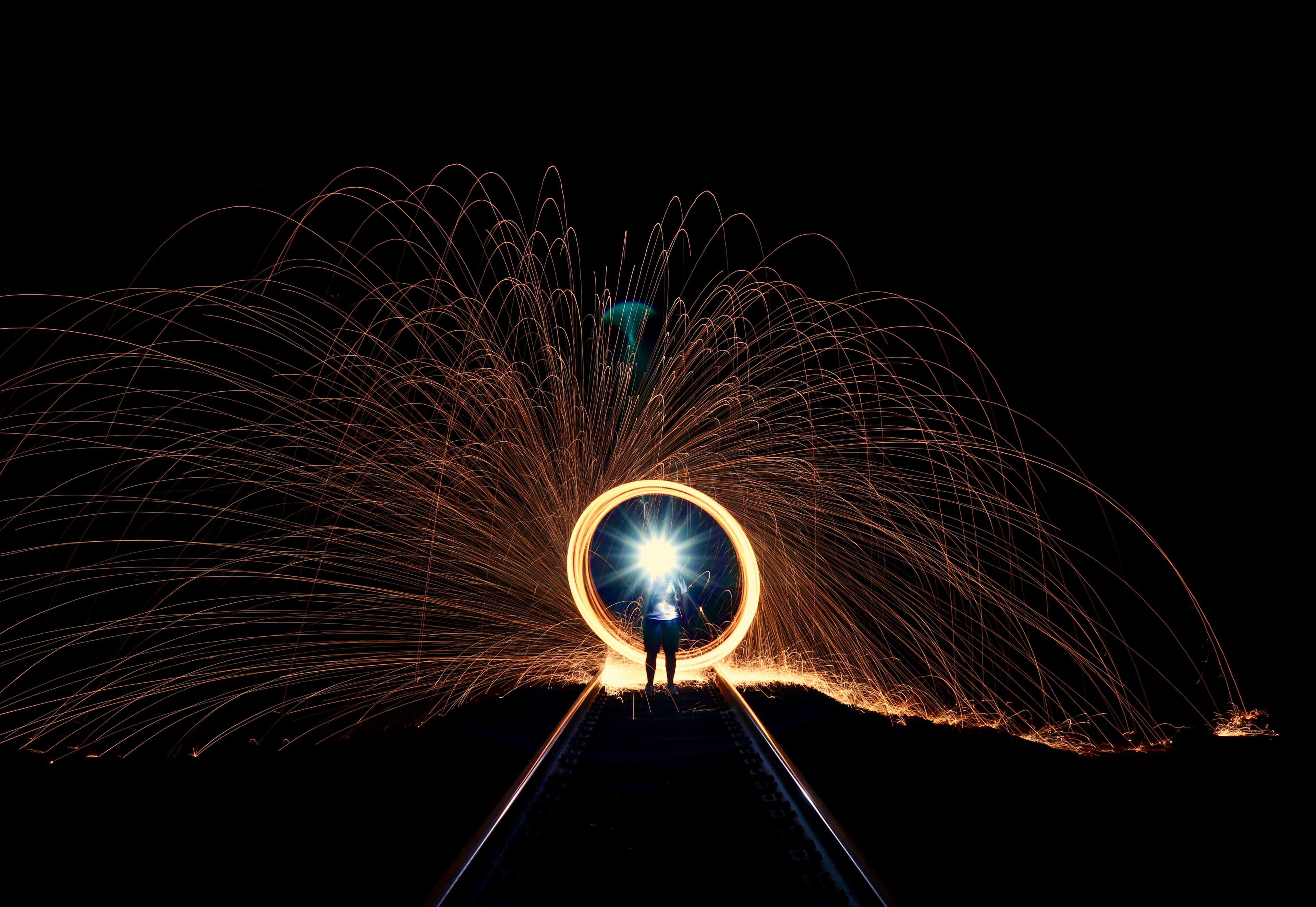 Person creating a circle of sparks on train tracks at night HD Wallpaper