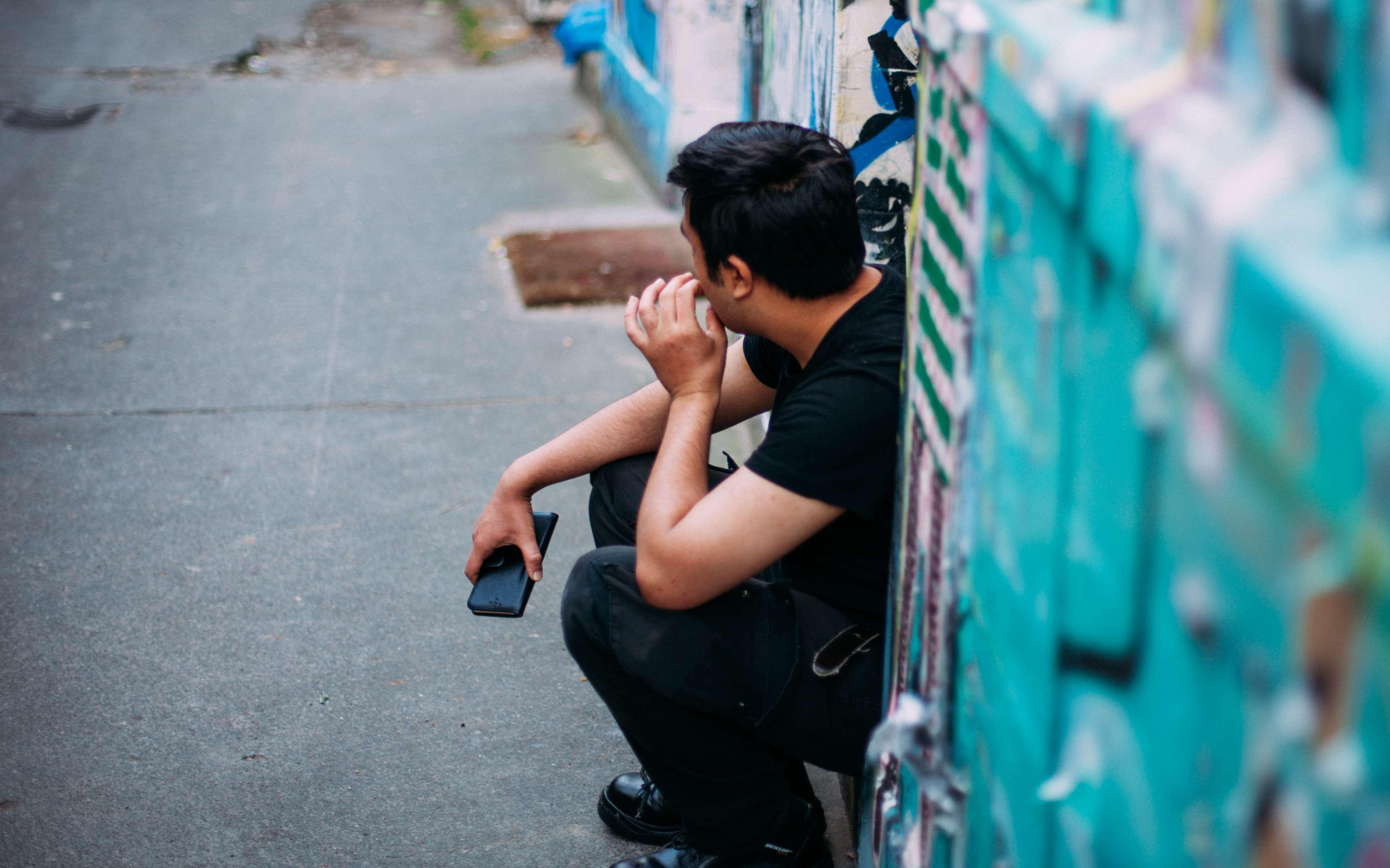Man sitting by graffiti wall with smartphone HD Wallpaper