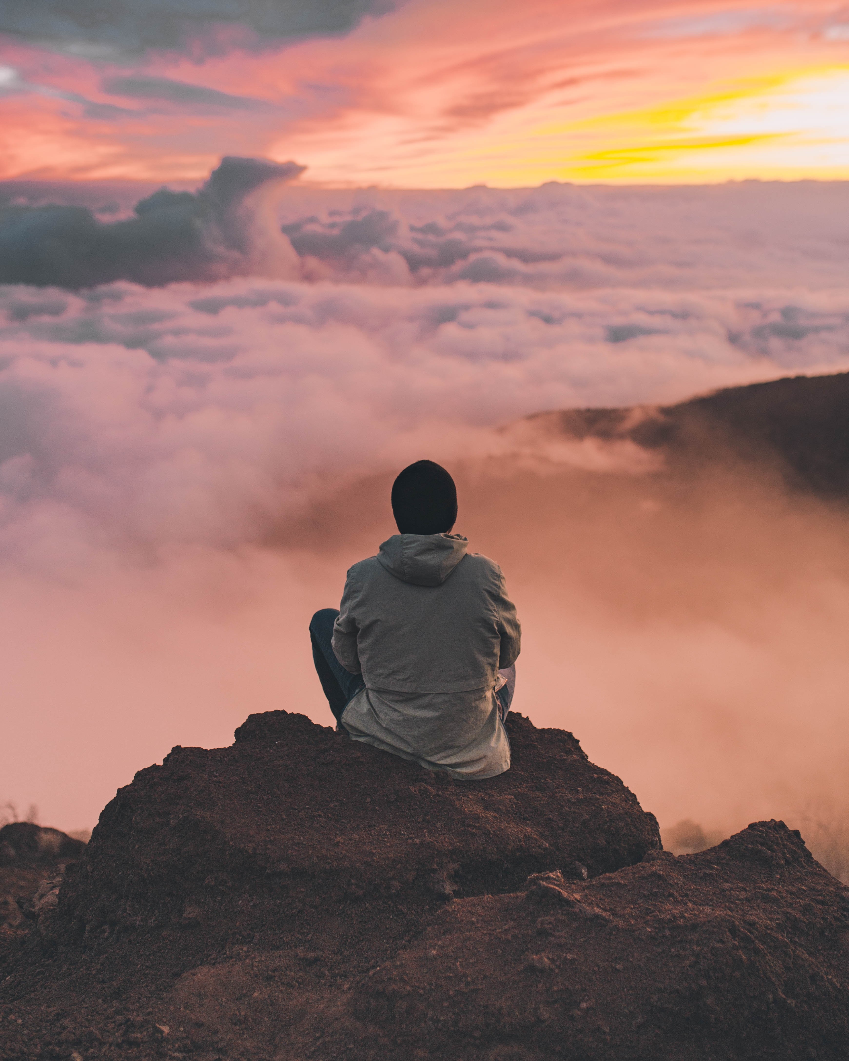 Man sitting on a rock above clouds at sunset HD Wallpaper