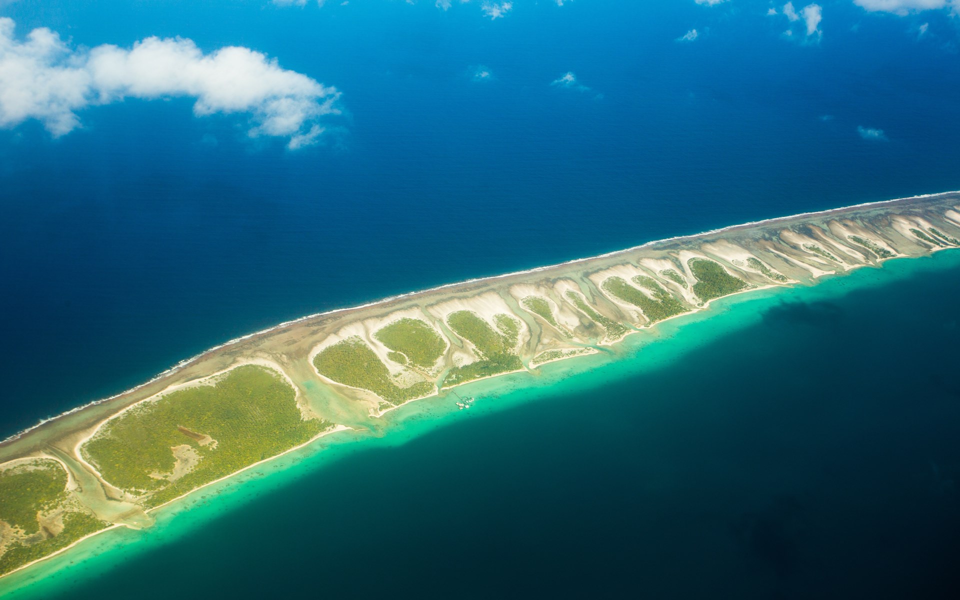 Aerial view of a long, narrow island with green vegetation and turquoise water HD Wallpaper