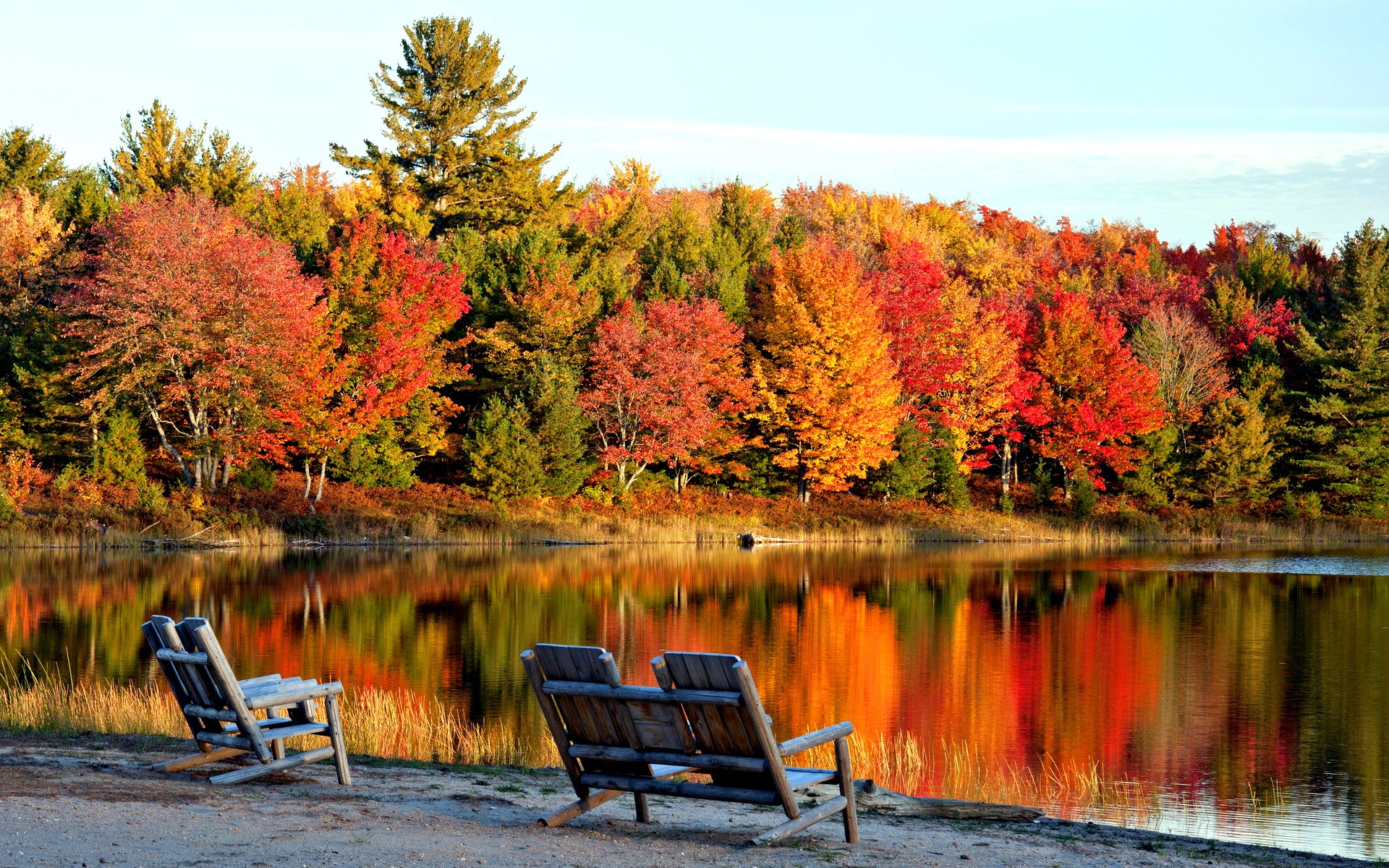 Two wooden chairs by a lake with autumn trees HD Wallpaper