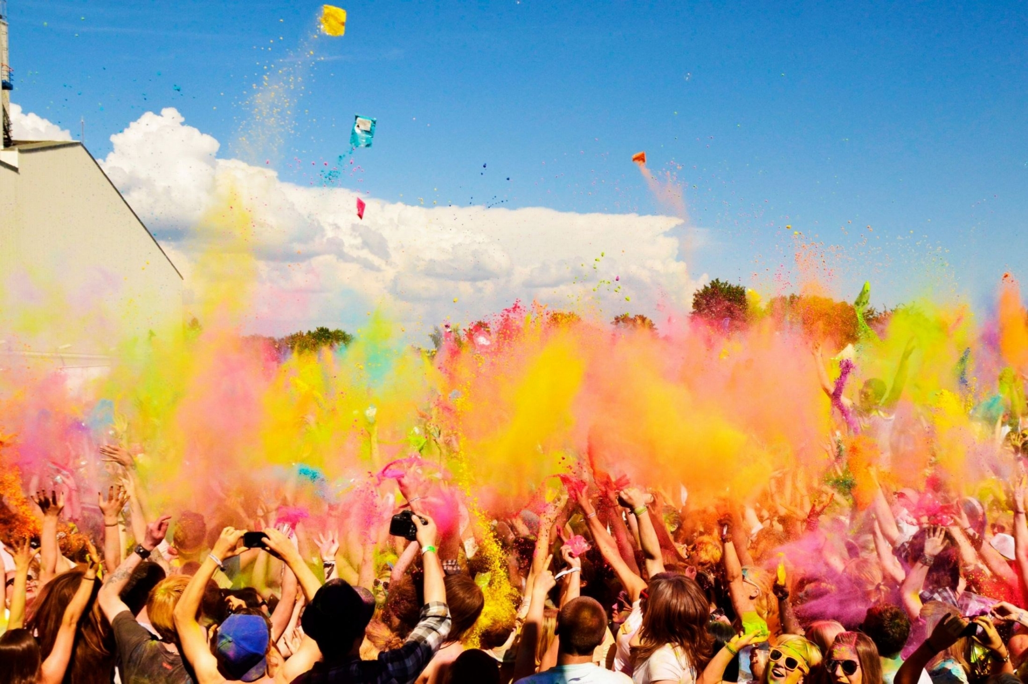 People celebrating with colorful powder under a blue sky HD Wallpaper