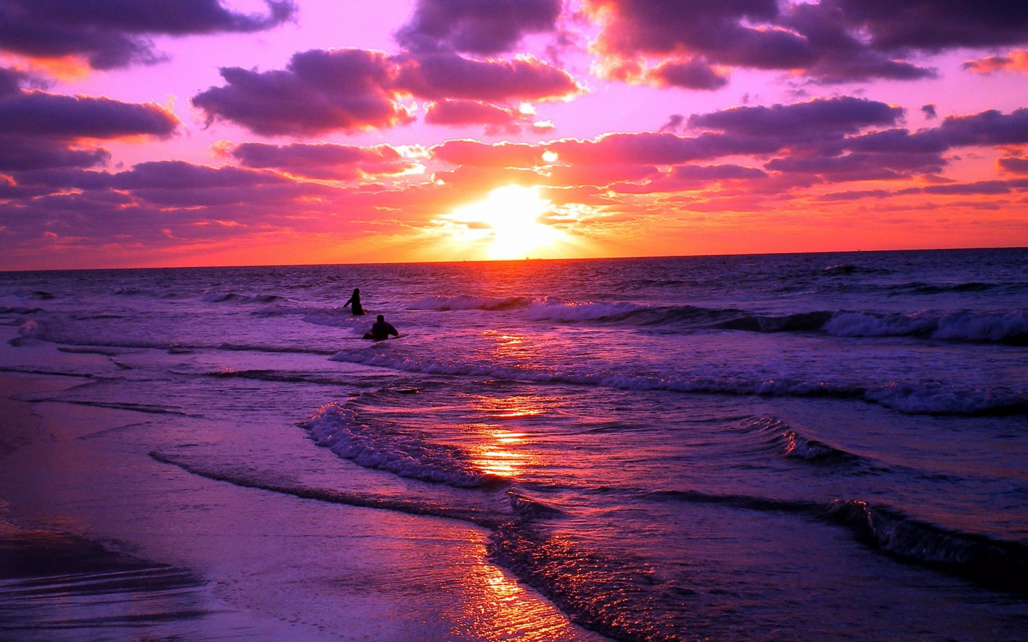 Sunset over the ocean with two people in the water HD Wallpaper