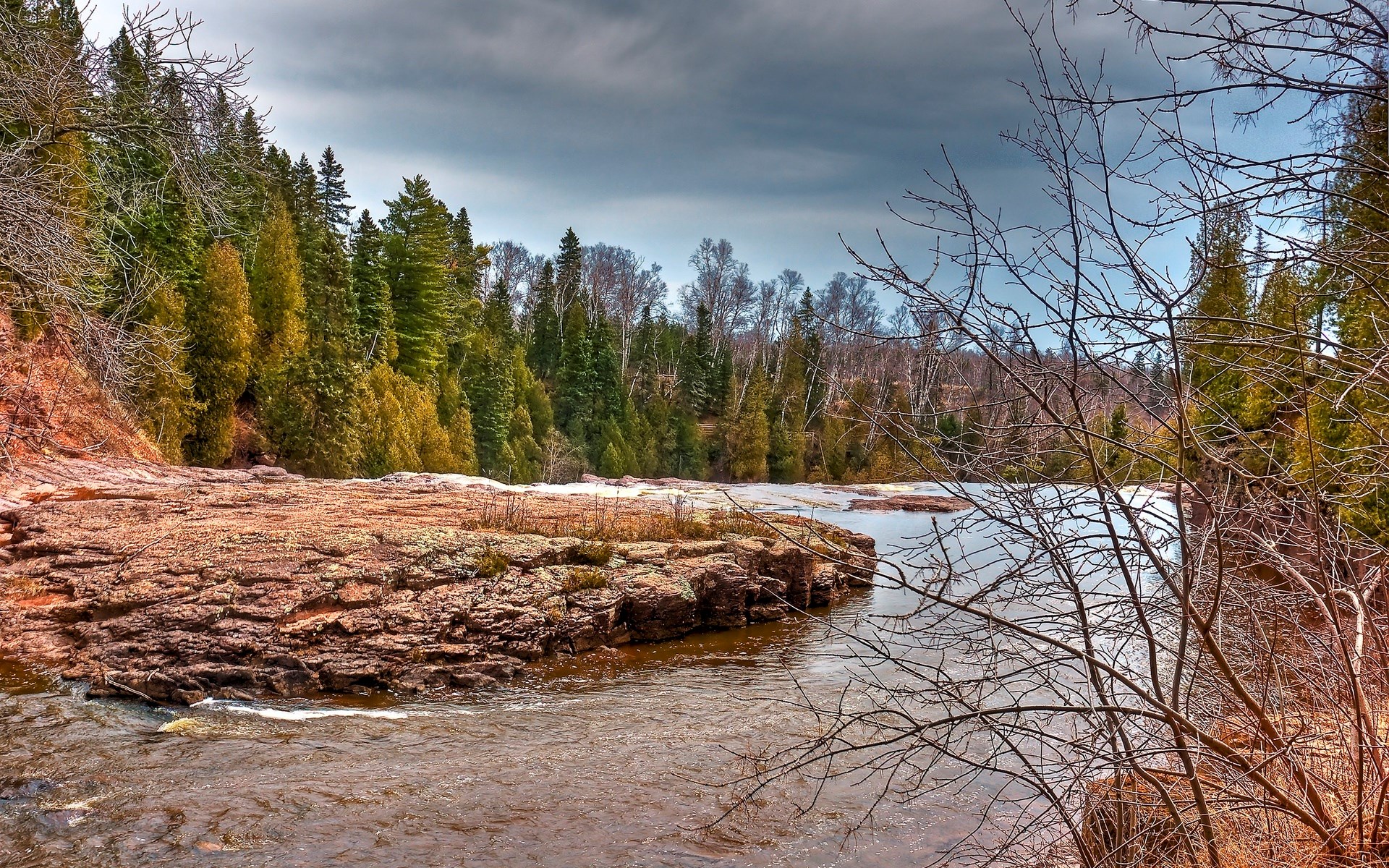 River flowing past rocky shore and evergreen forest HD Wallpaper