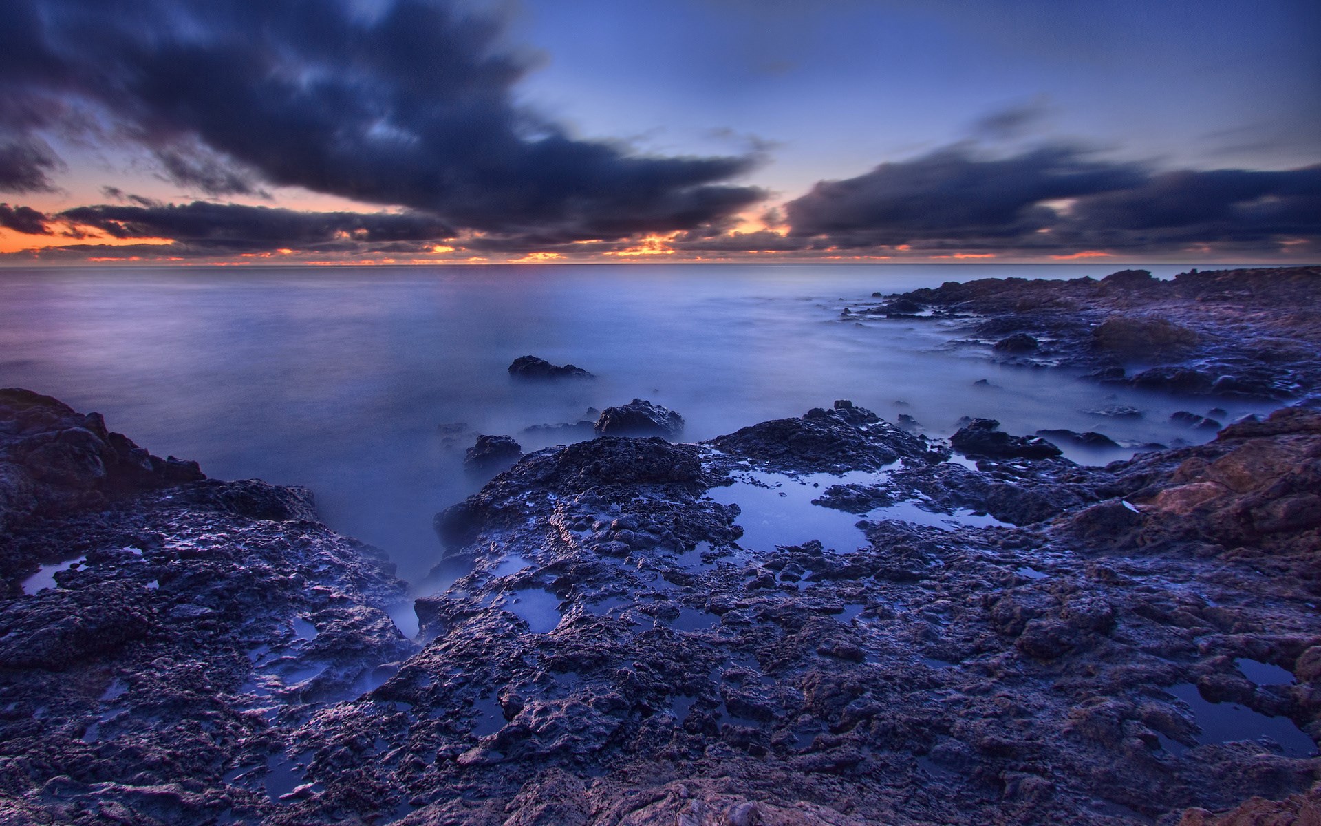 Rocky coastline at dusk with ocean waves HD Wallpaper