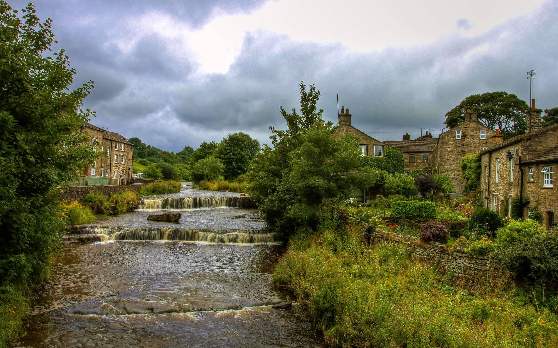 Stone village with cascading river and trees HD Wallpaper