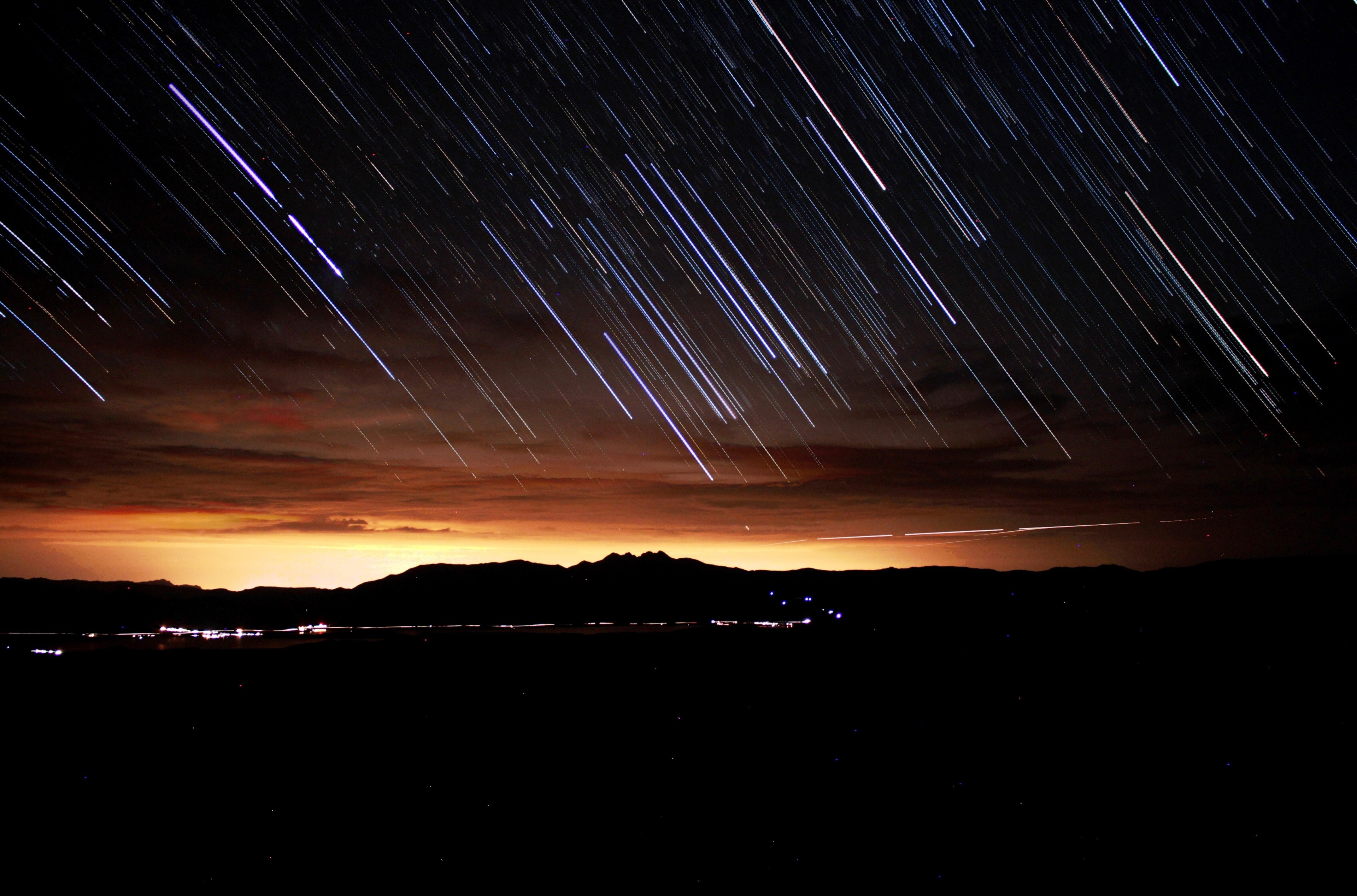 Star trails over mountains and city lights at night HD Wallpaper