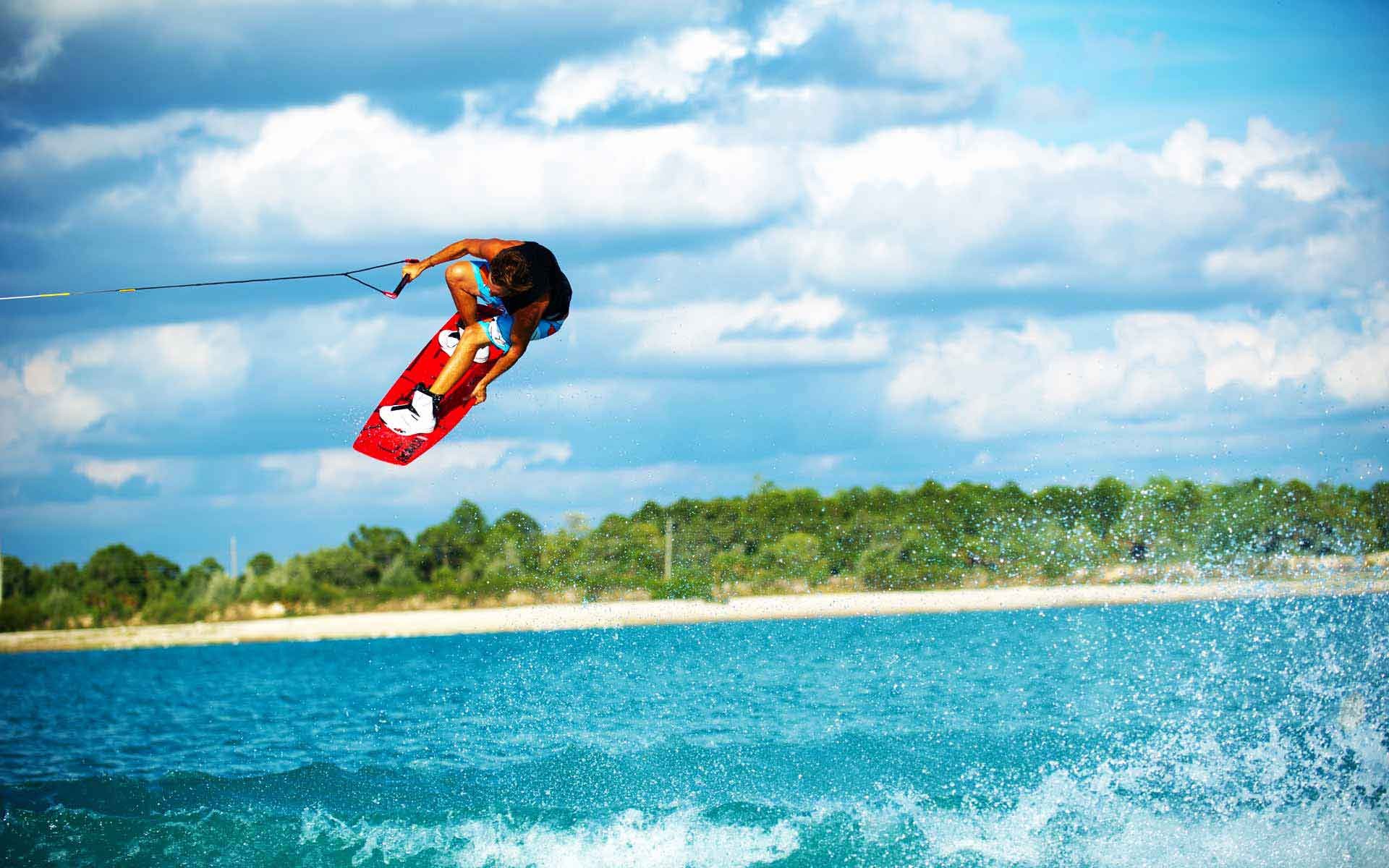 Wakeboarder jumping over water with trees in background HD Wallpaper