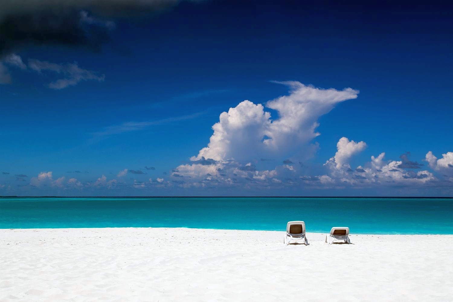 Two lounge chairs on a white sand beach with turquoise water and blue sky HD Wallpaper
