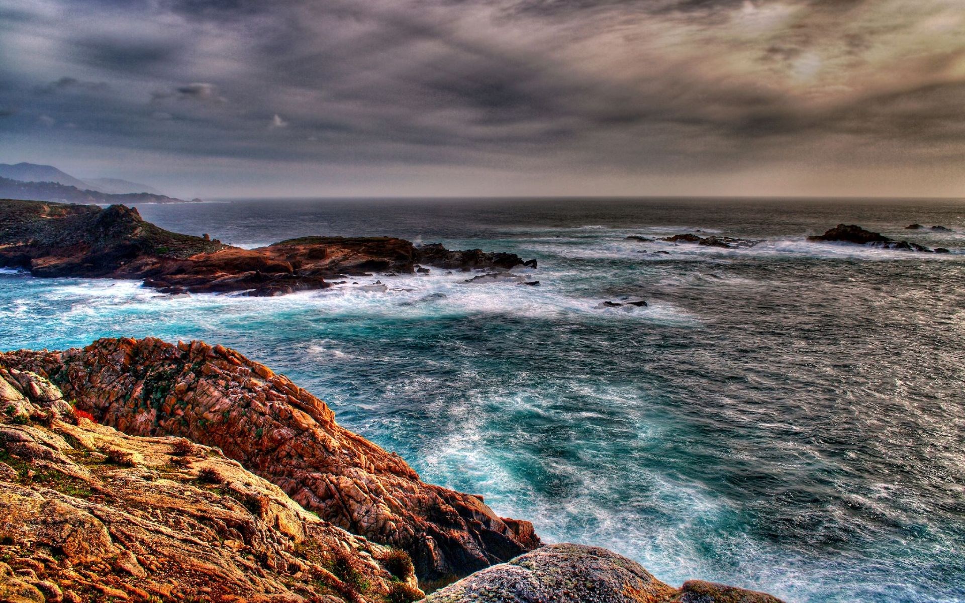 Rocky coastline with crashing waves under a cloudy sky HD Wallpaper