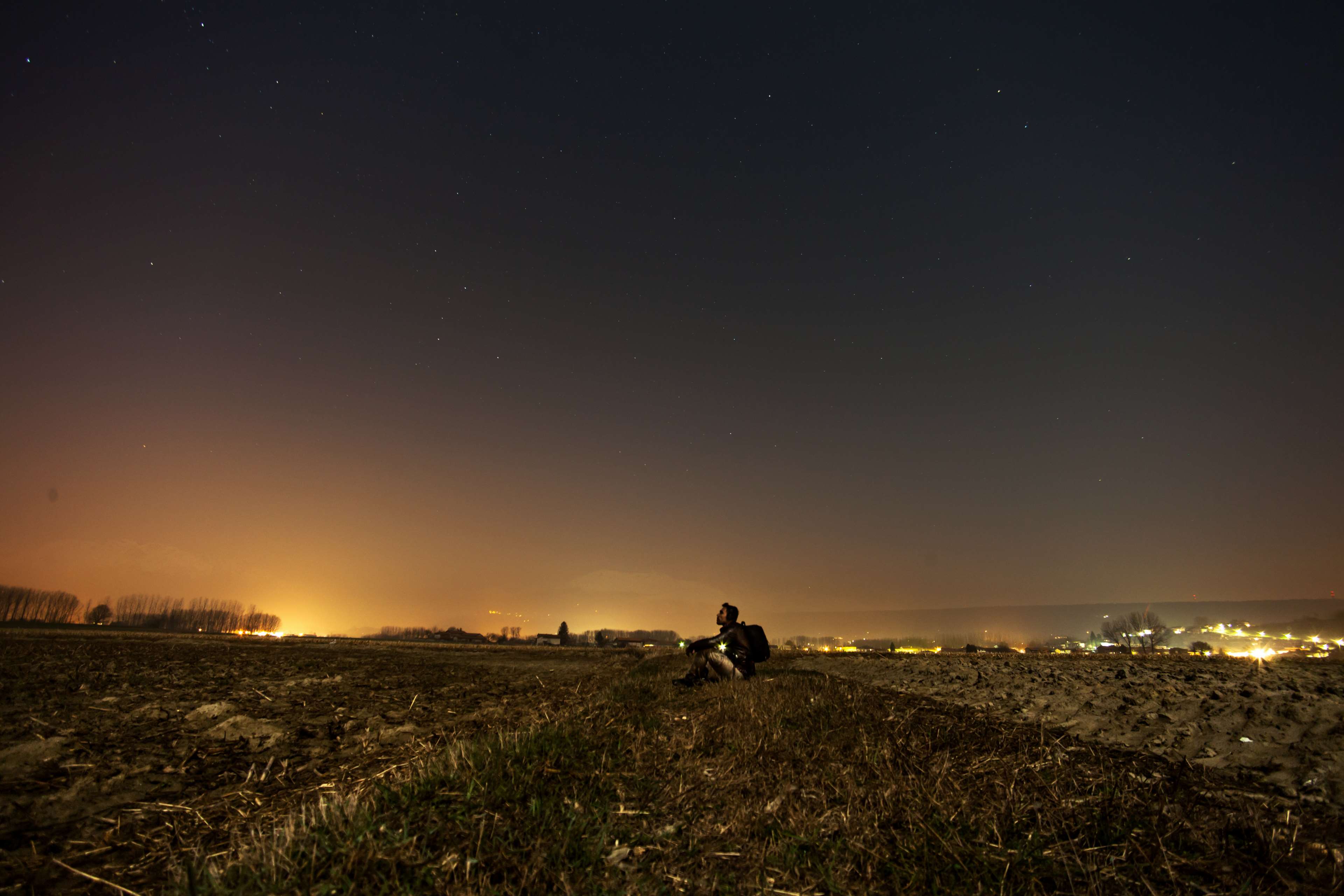 Man sitting in a field at night under starry sky HD Wallpaper