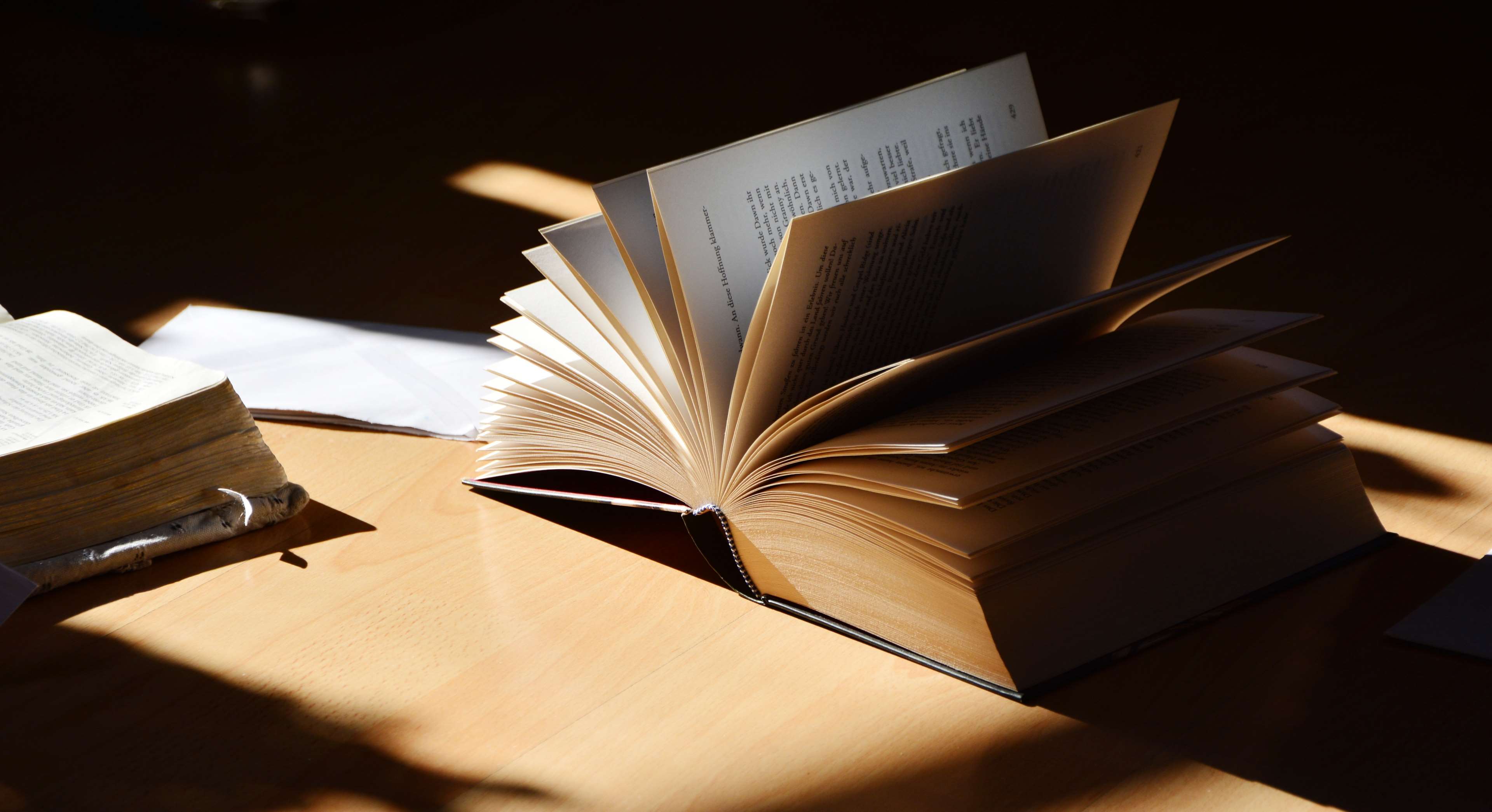 Open book with pages fanned out on a wooden table HD Wallpaper