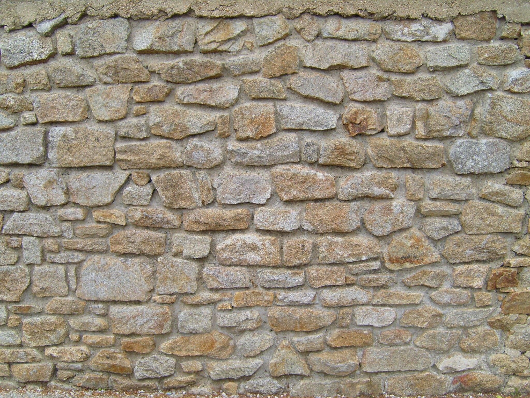 A textured wall made of rough, irregular stones. HD Wallpaper