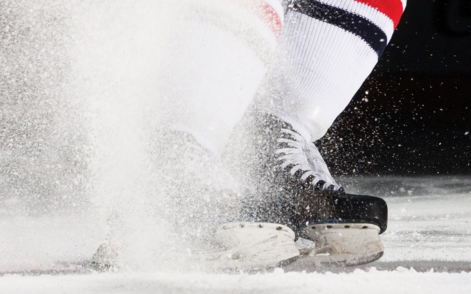 Hockey player skates on ice, kicking up snow HD Wallpaper
