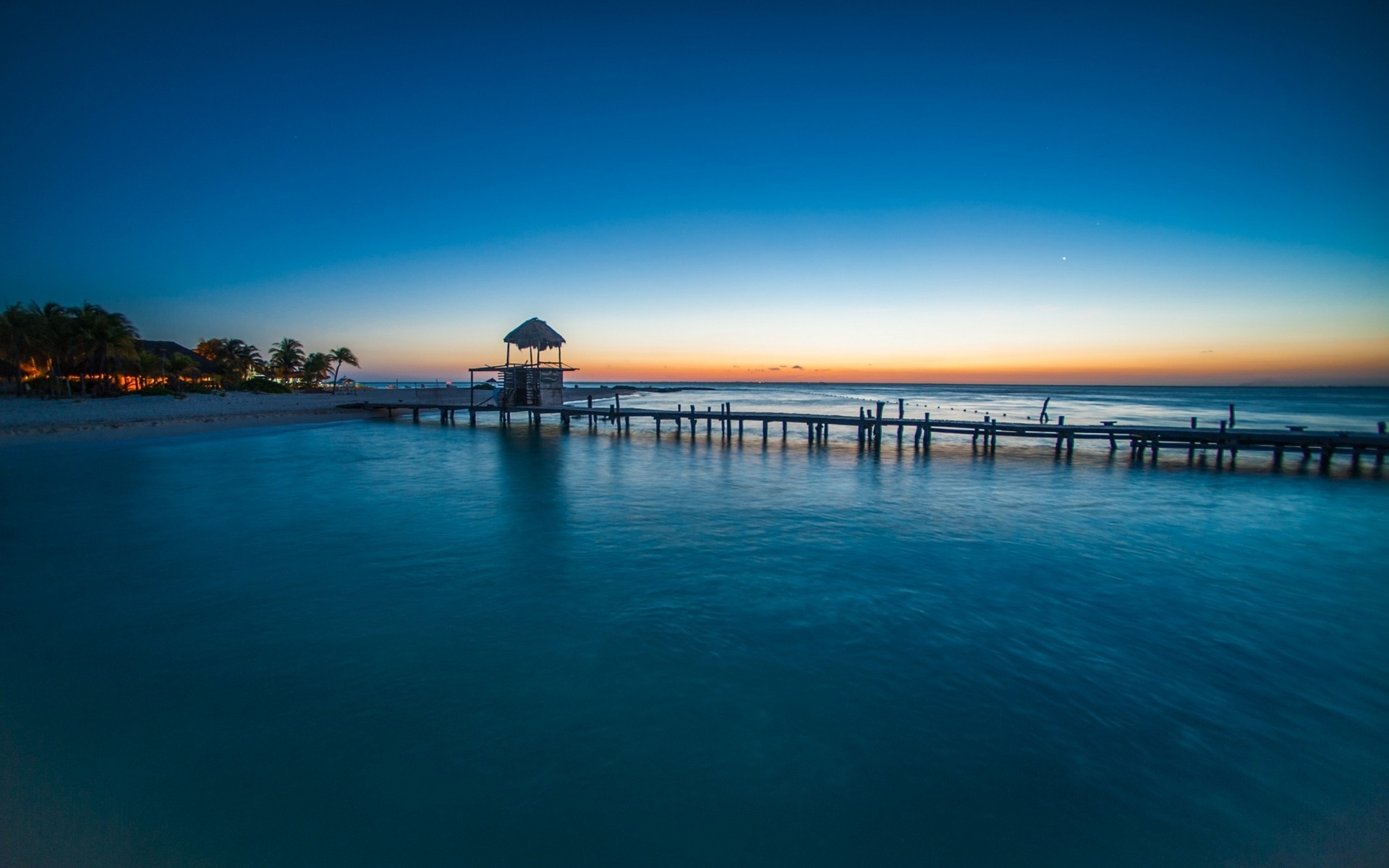 Tropical beach pier at sunset with ocean and palm trees HD Wallpaper