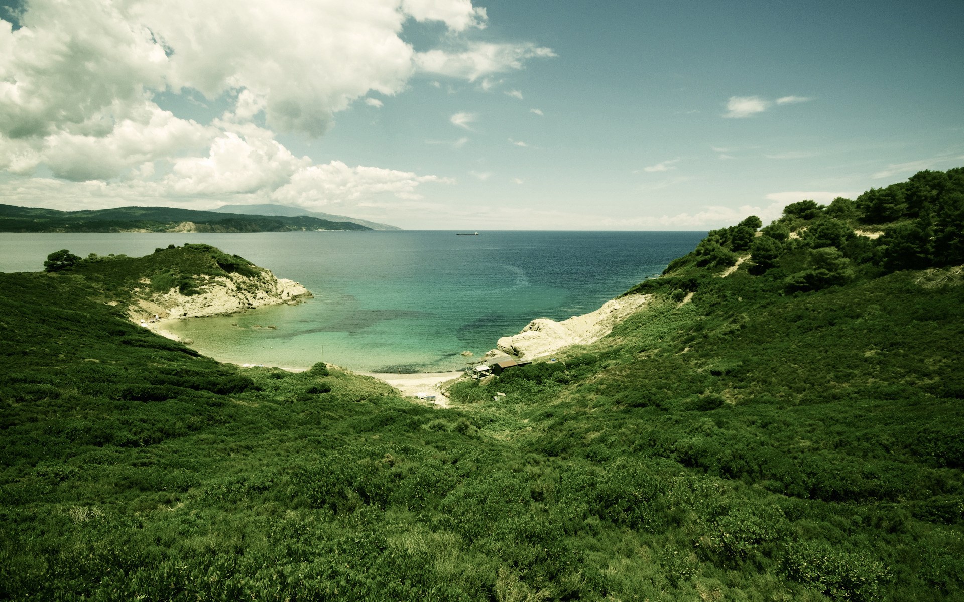 Green hills overlooking a bay with turquoise water HD Wallpaper