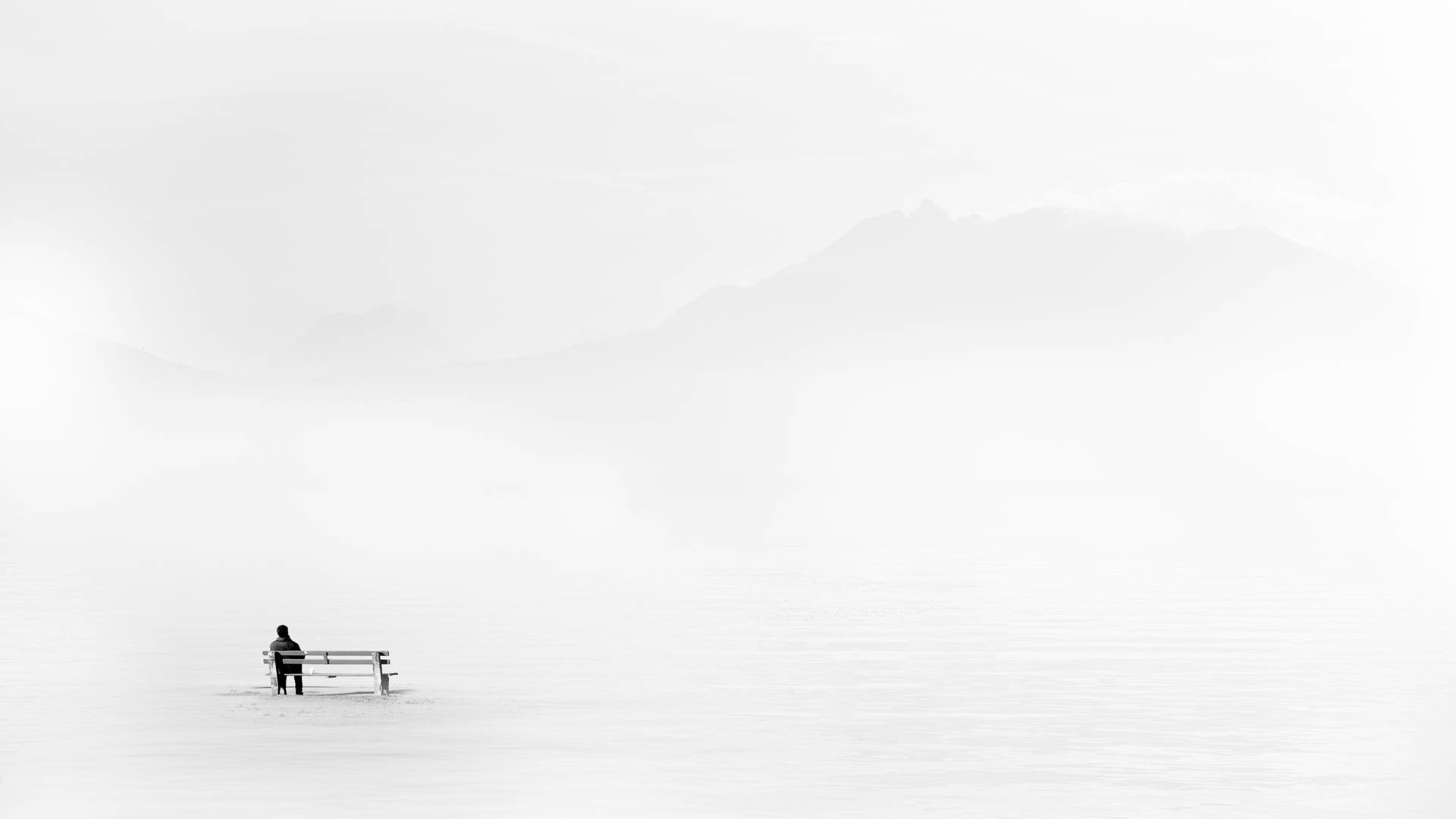 Man sitting on a bench in a snowy landscape with mountains HD Wallpaper