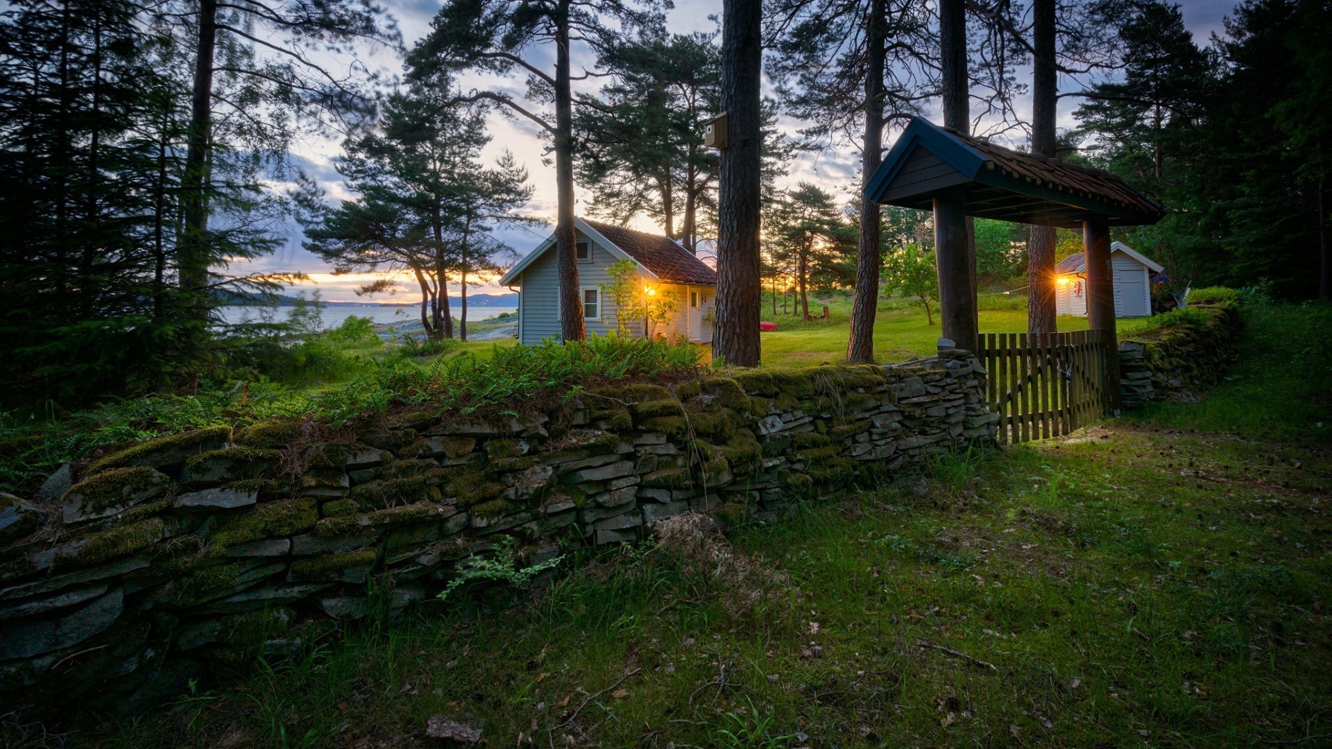 Stone wall and gate leading to a house by a lake at sunset HD Wallpaper