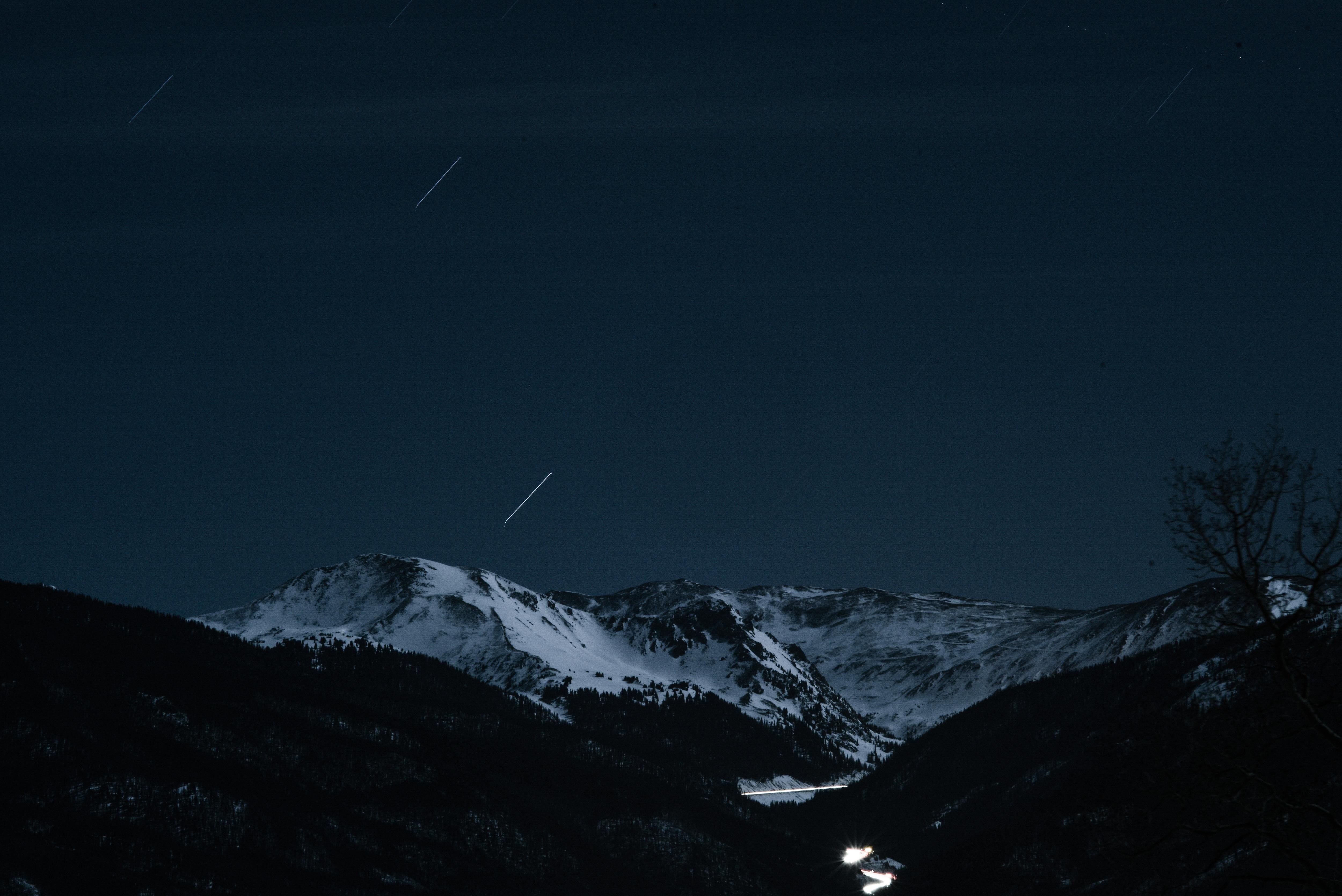 Snowy mountains under a starry night sky with light trails HD Wallpaper