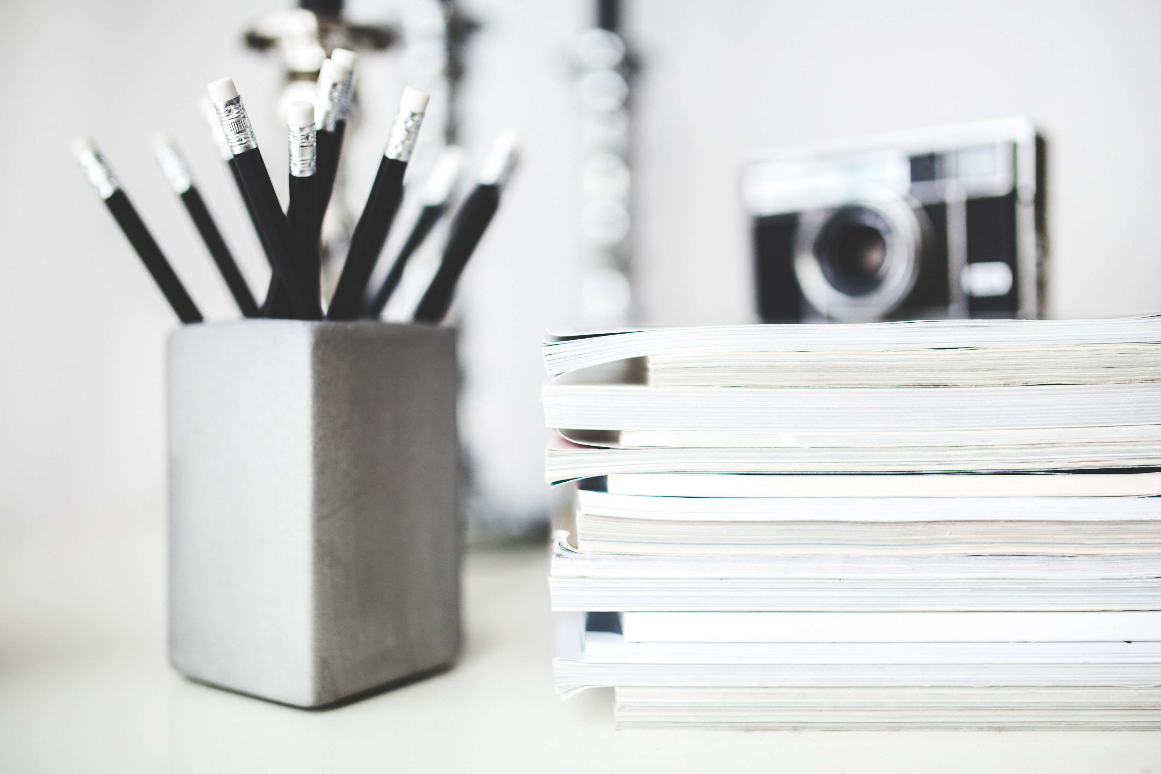 Pencils in a holder, stack of magazines, and camera on a desk HD Wallpaper