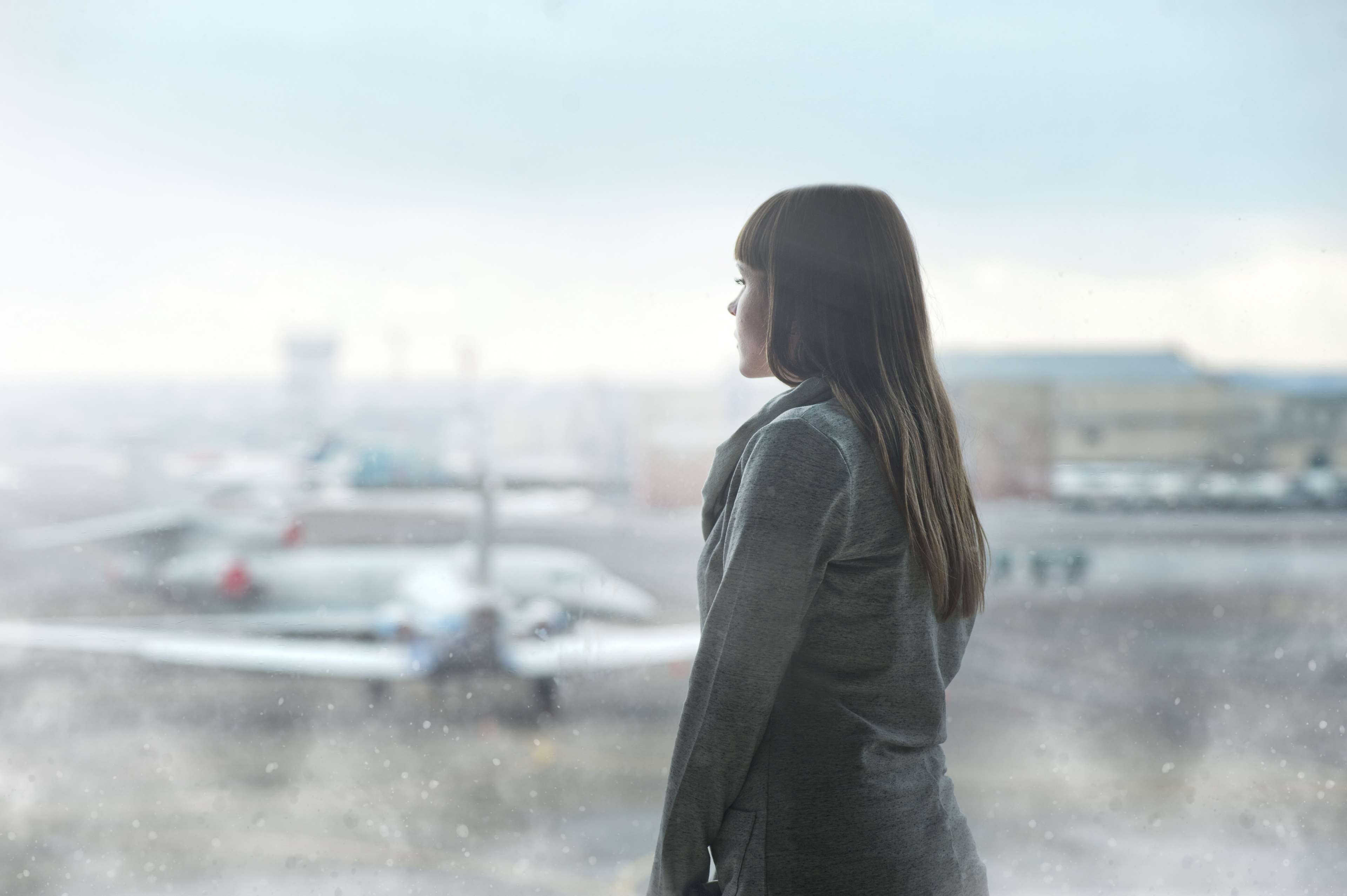 Woman looking out airport window at airplanes HD Wallpaper