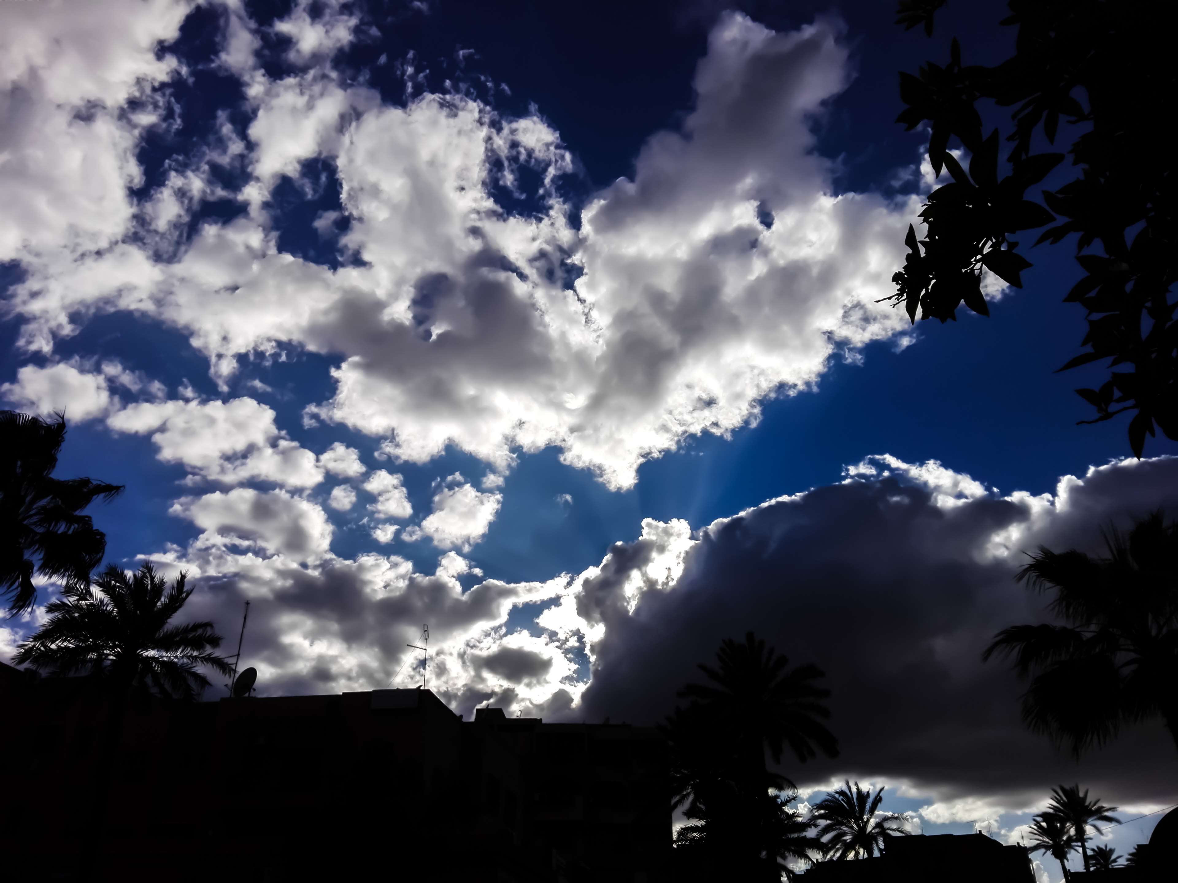 Dramatic clouds over silhouetted buildings and palm trees in Morocco HD Wallpaper
