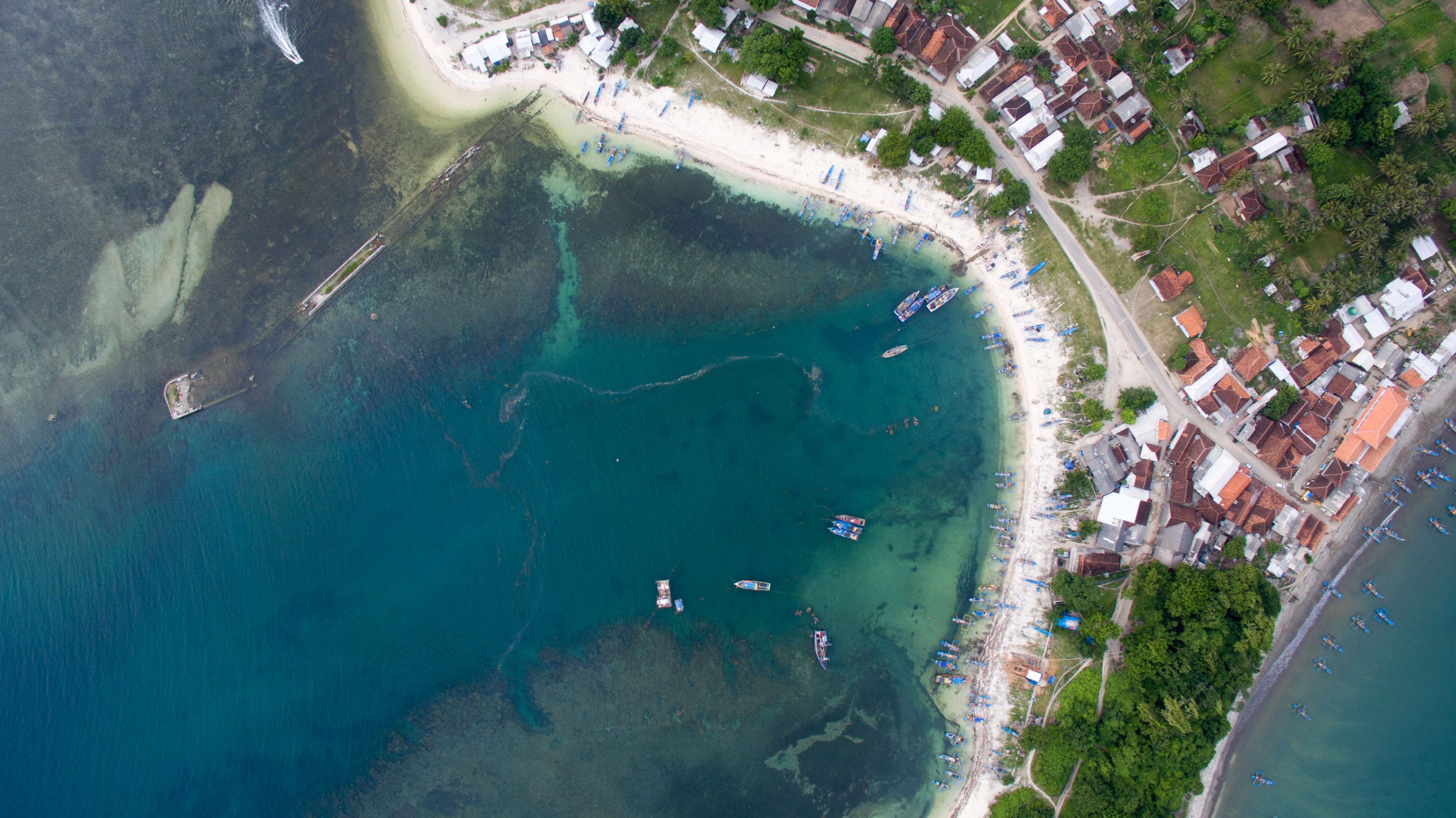 Aerial view of a coastal village with boats and a beach HD Wallpaper