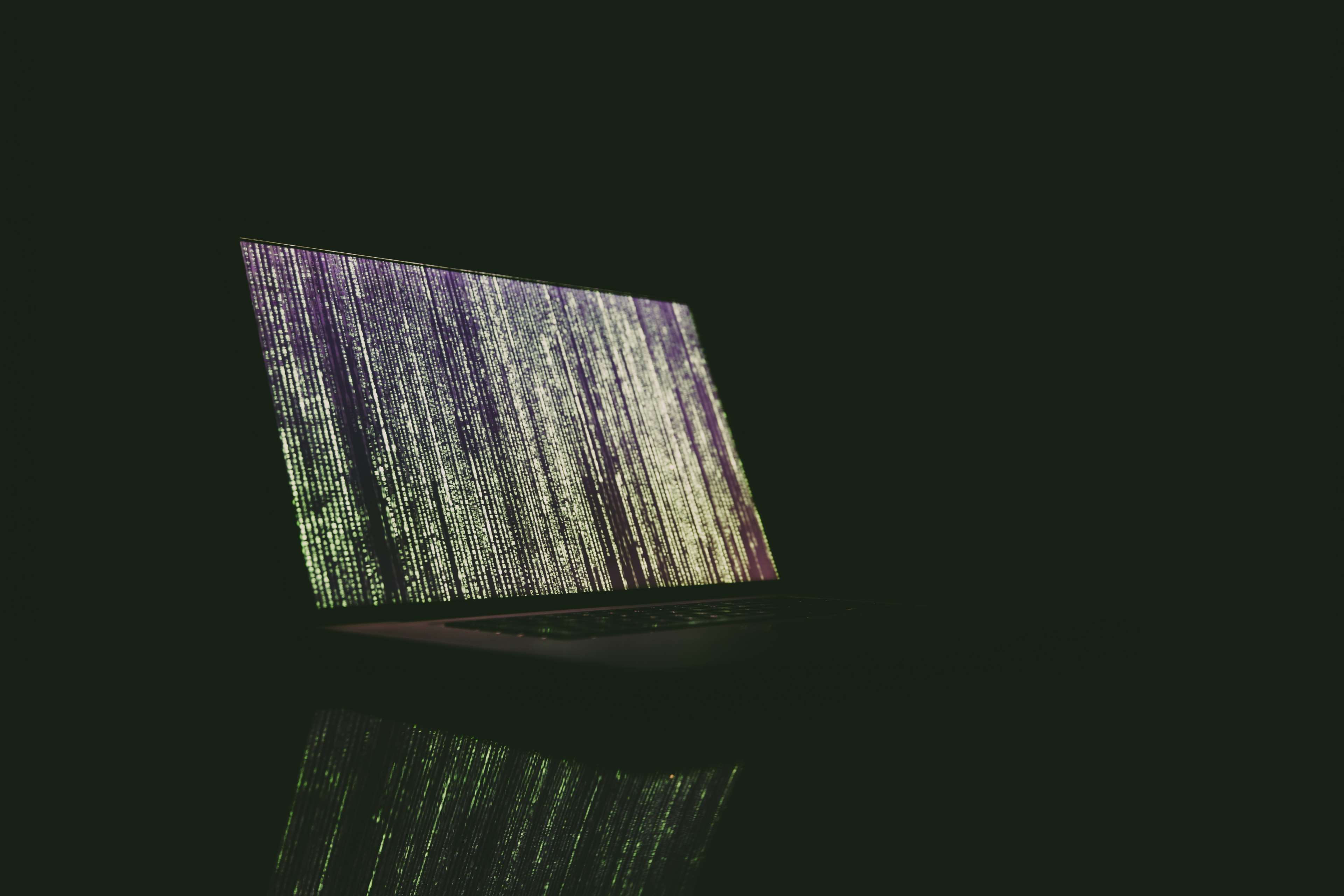 Laptop displaying matrix code in dark room 4K HD Wallpaper