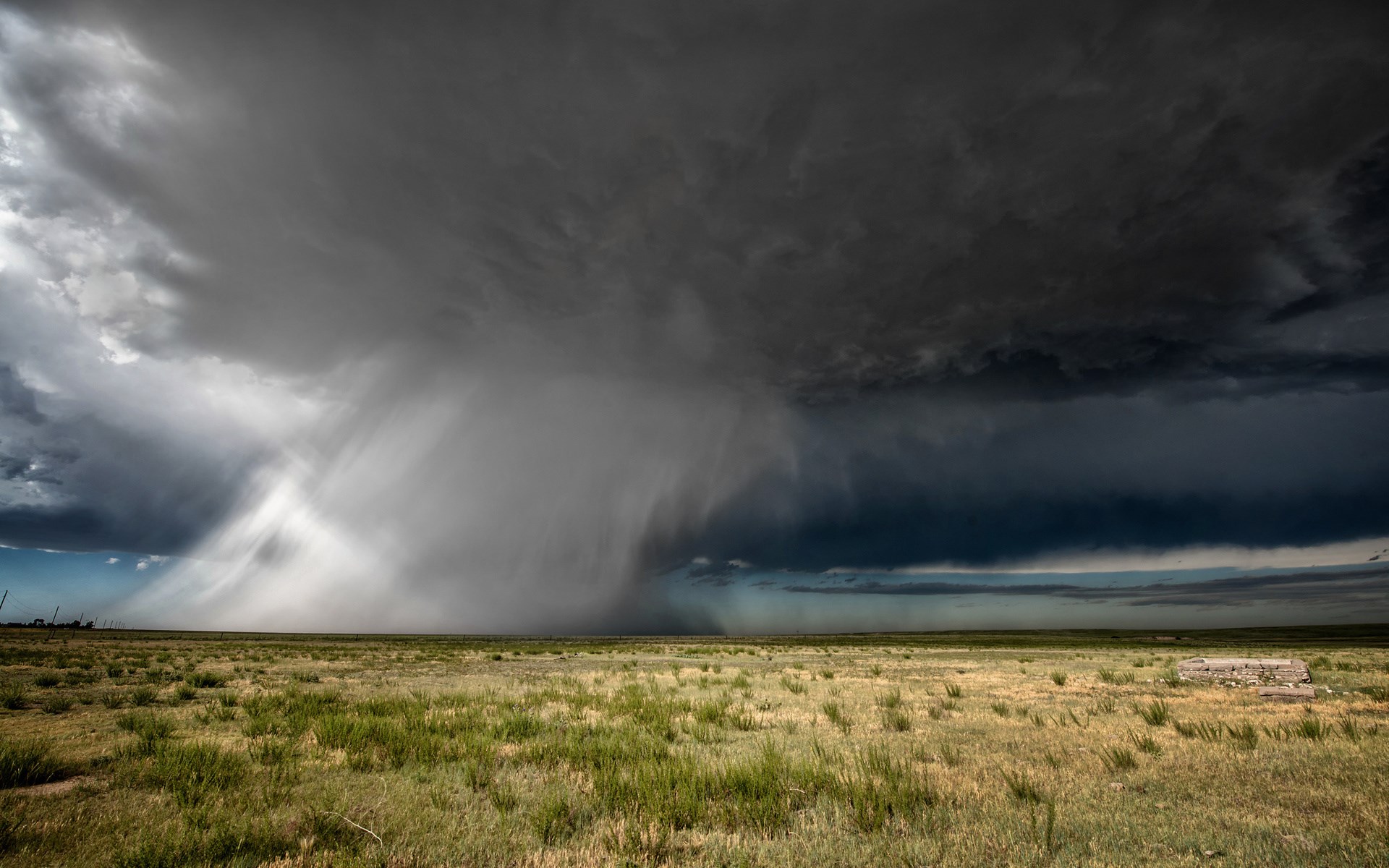 Storm clouds over a grassy plain with debris HD Wallpaper